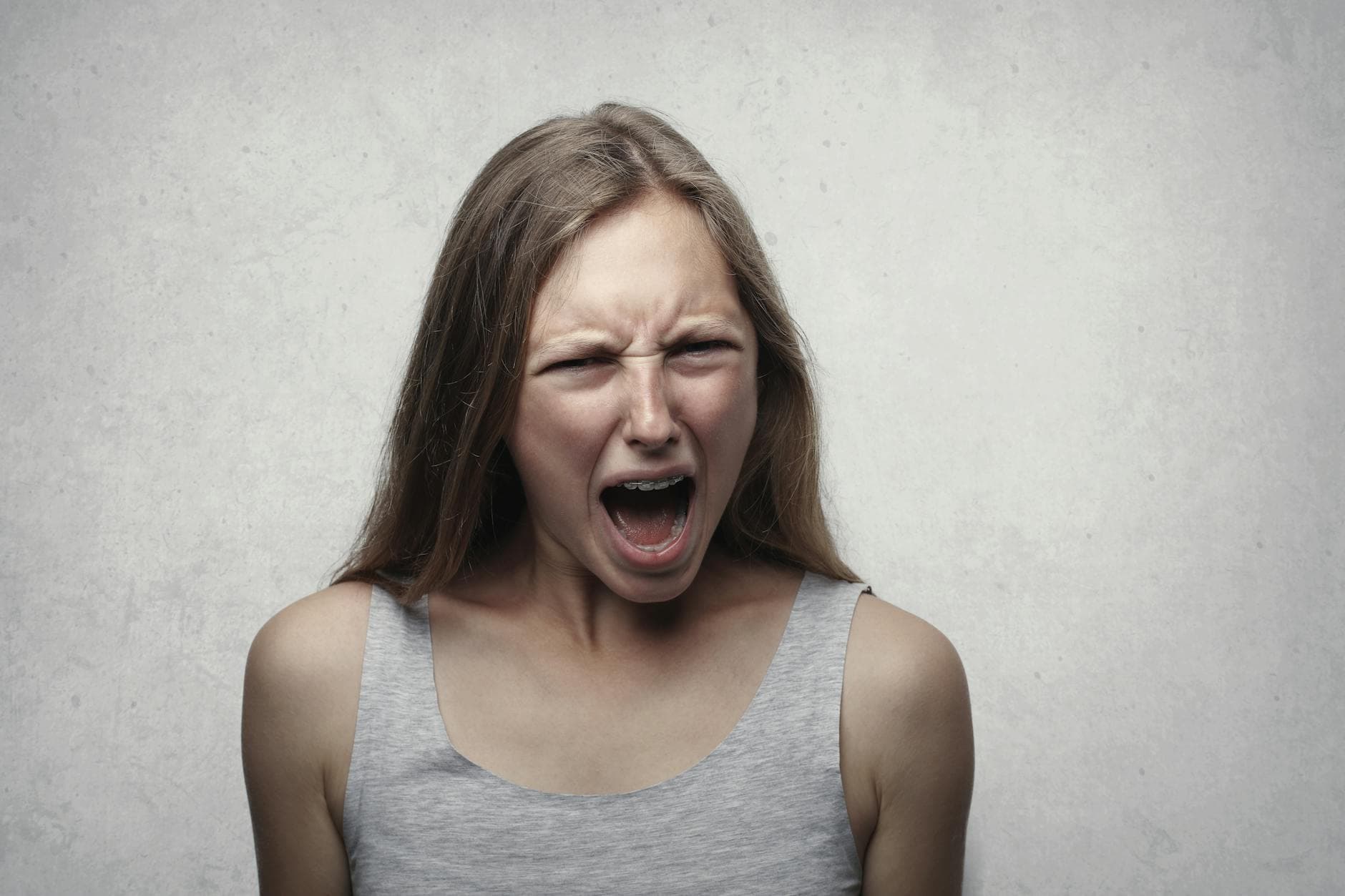 A woman with an intense facial expression screaming against a neutral gray background. - anger management classes