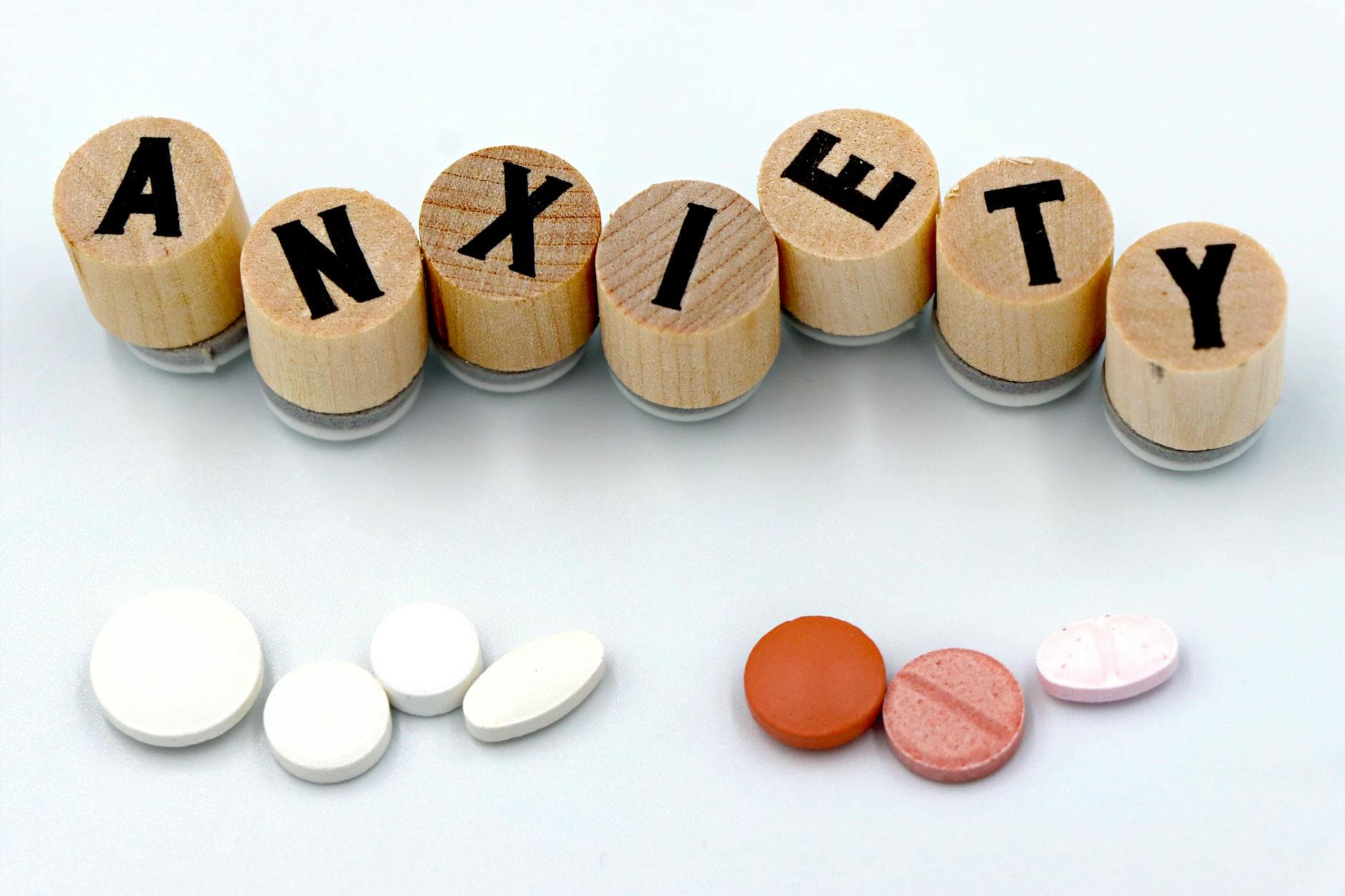 Wooden blocks spelling 'Anxiety' with assorted pills below on a light background. - anxiety and depression treatment
