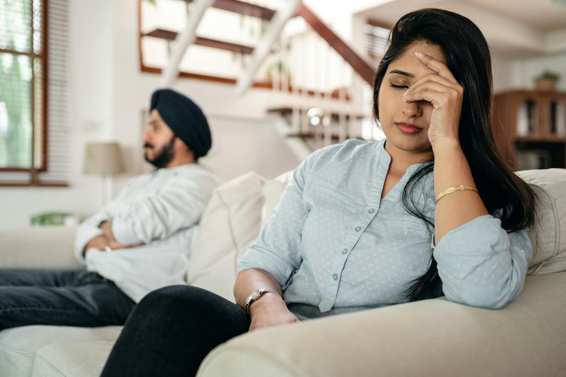 A young couple sitting on a couch indoors, showing signs of stress and frustration. - anxiety in romantic relationships