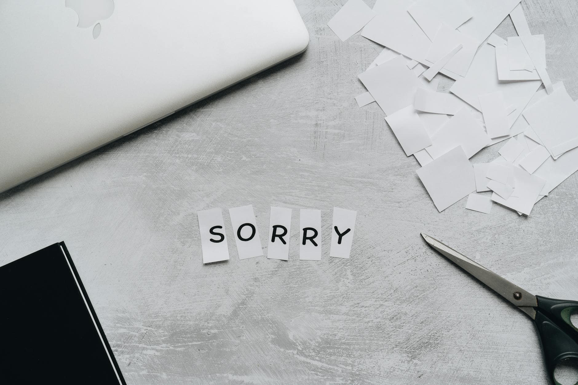 Top view of a desk with cut-out letters spelling 'sorry', scissors, and a laptop. - how to apologize professionally