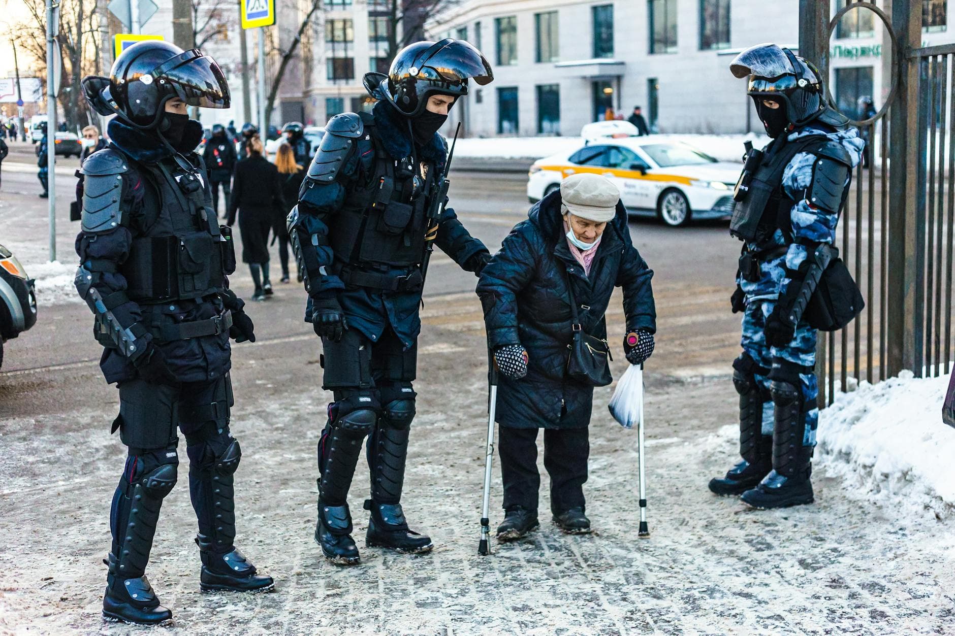 Police officers in riot gear help an elderly woman navigate a snowy street. - children's empathy winter service