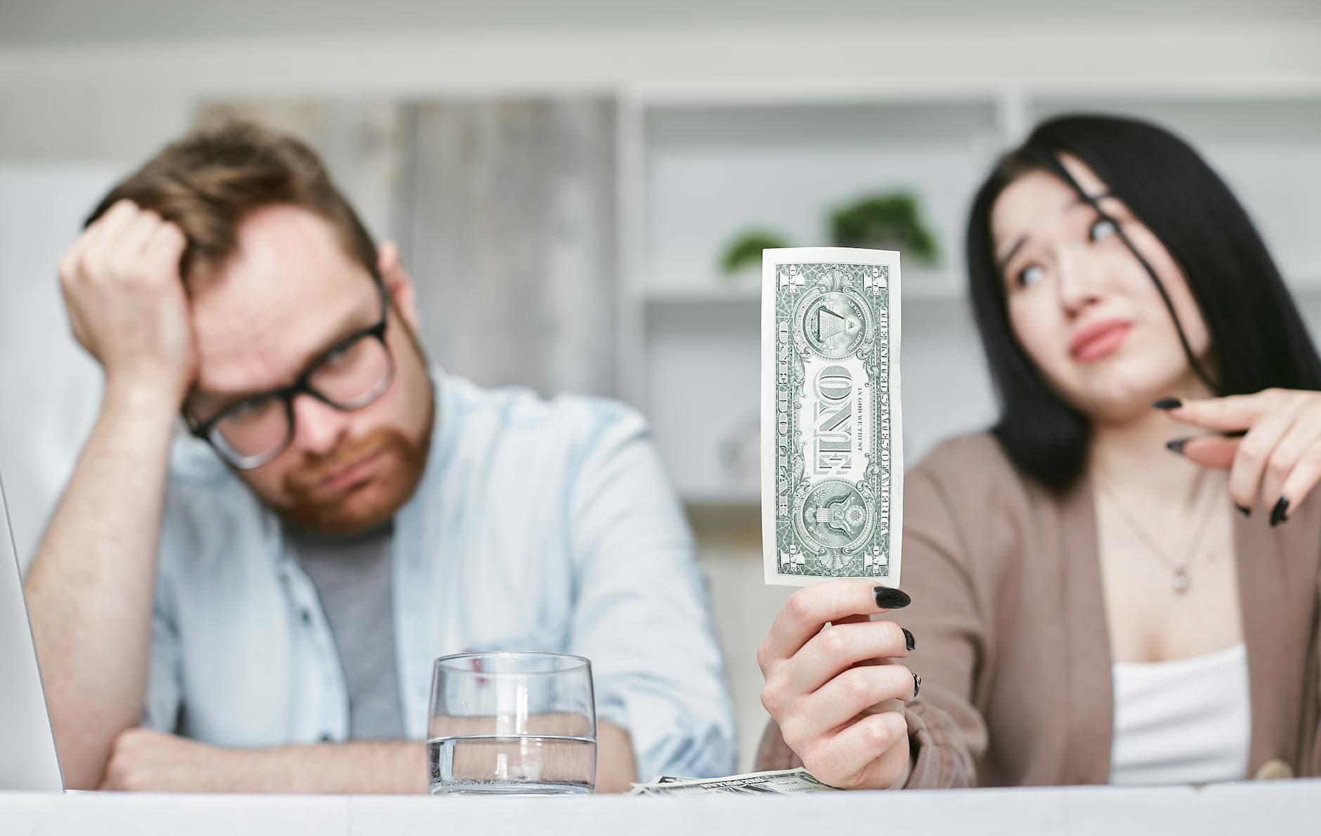 An adult interracial couple expressing concern about finances as they hold a one dollar bill indoors. - couples financial stress communication
