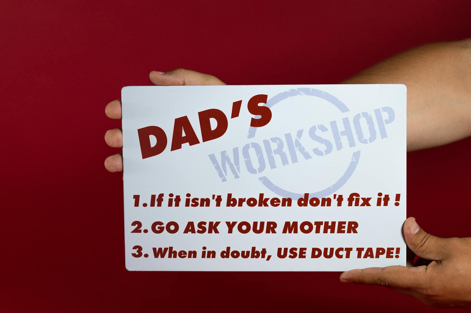Close-up of a humorous sign with Dad's workshop rules on a red background held by hands. - funny advice for newlyweds