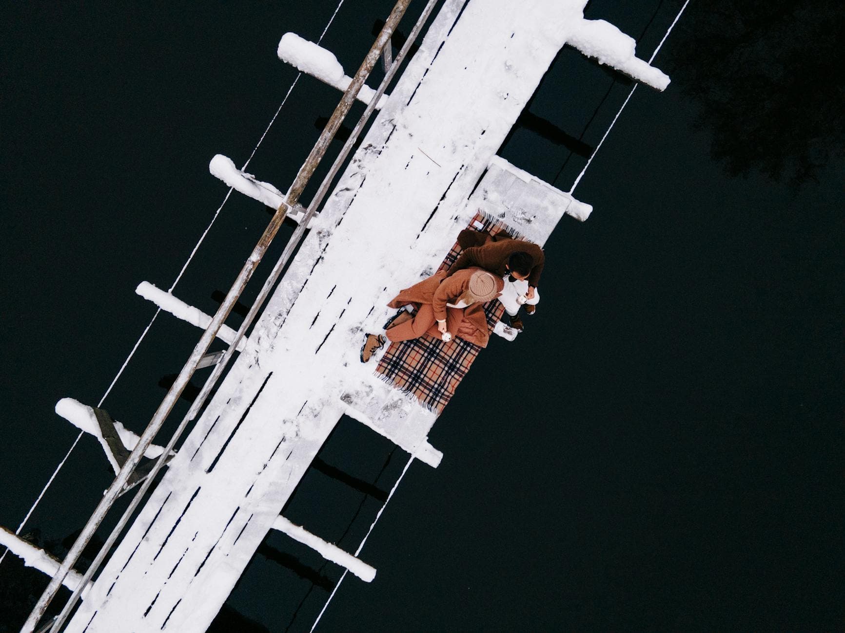 A romantic winter scene of a couple cuddling on a pier covered in snow, surrounded by water. - intimate winter date ideas