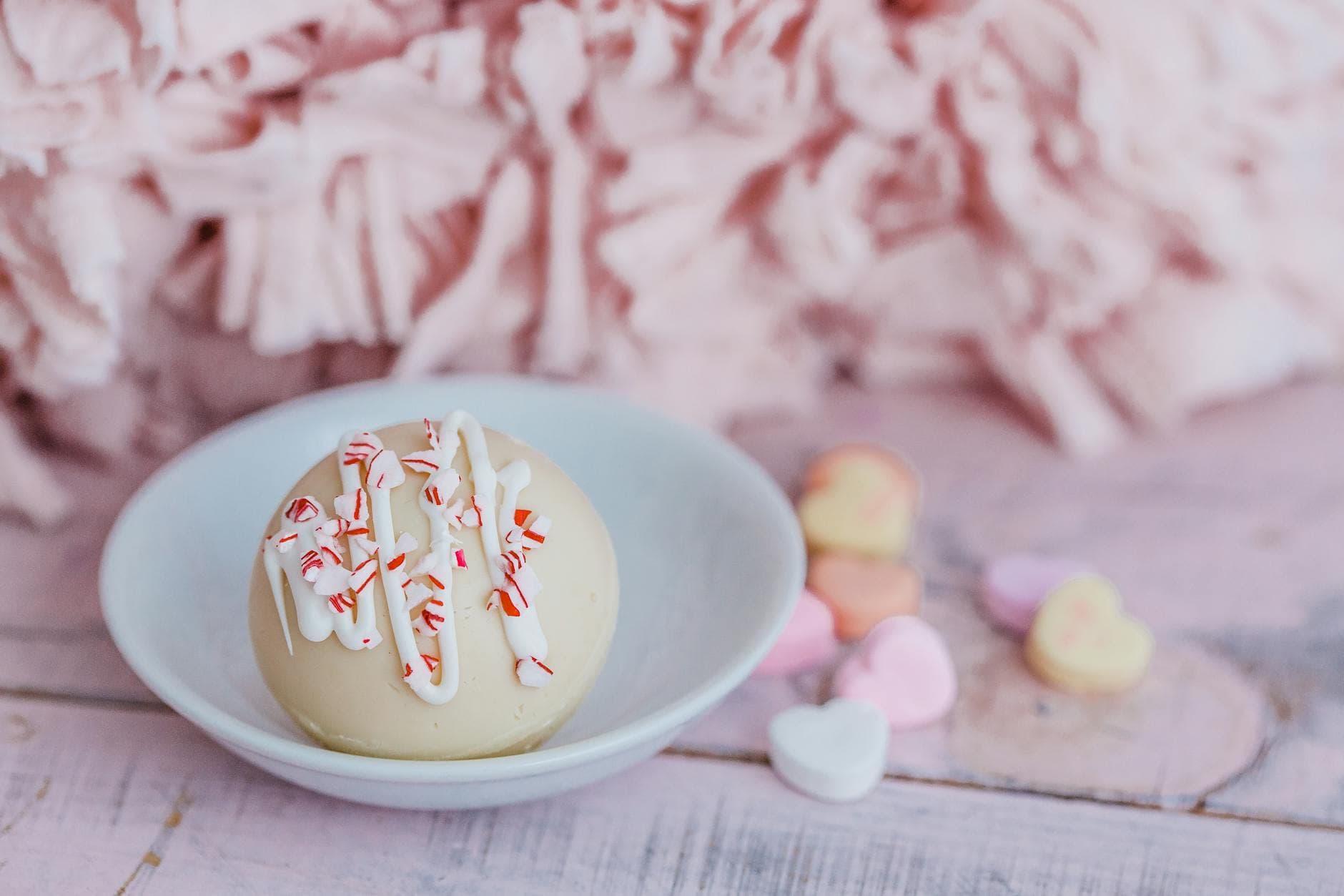 A delicious hot cocoa bomb with peppermint sprinkles, surrounded by heart-shaped candies, perfect for a sweet treat. - love bombing meaning