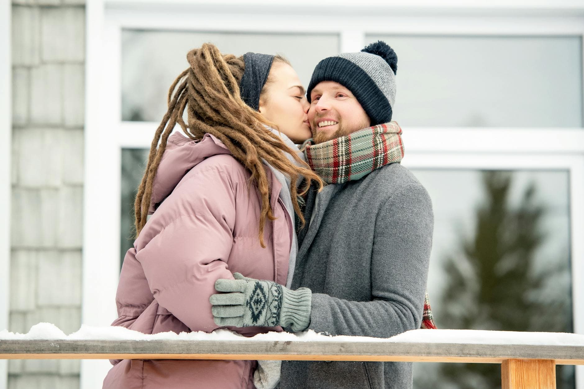 A couple shares a warm kiss outdoors in a cozy winter setting. - winter happiness couples