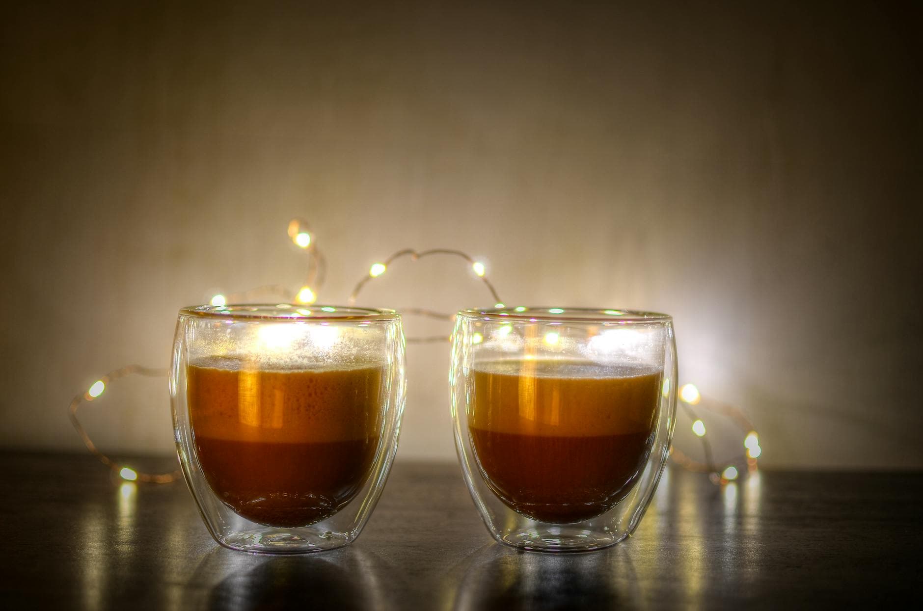 Two cappuccinos in double-walled glasses with festive lights. - winter mood boost activities