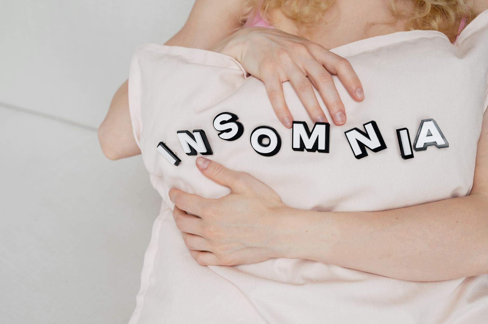 Close-up of a woman holding a pillow with 'insomnia' text, depicting sleep disorder. - winter sleep problems