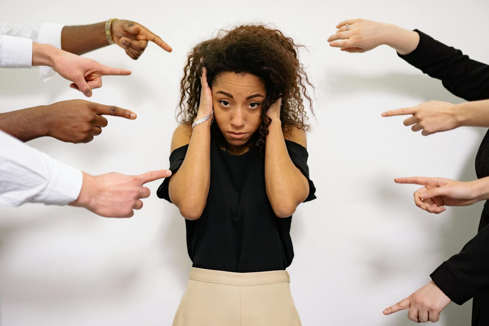 Stressed woman with hands on ears surrounded by pointing fingers, illustrating pressure. - winter social anxiety