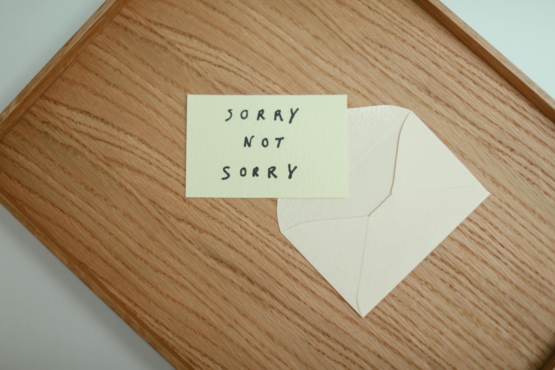 A flat lay of a 'Sorry Not Sorry' card with an envelope on a wooden surface. - write apology email