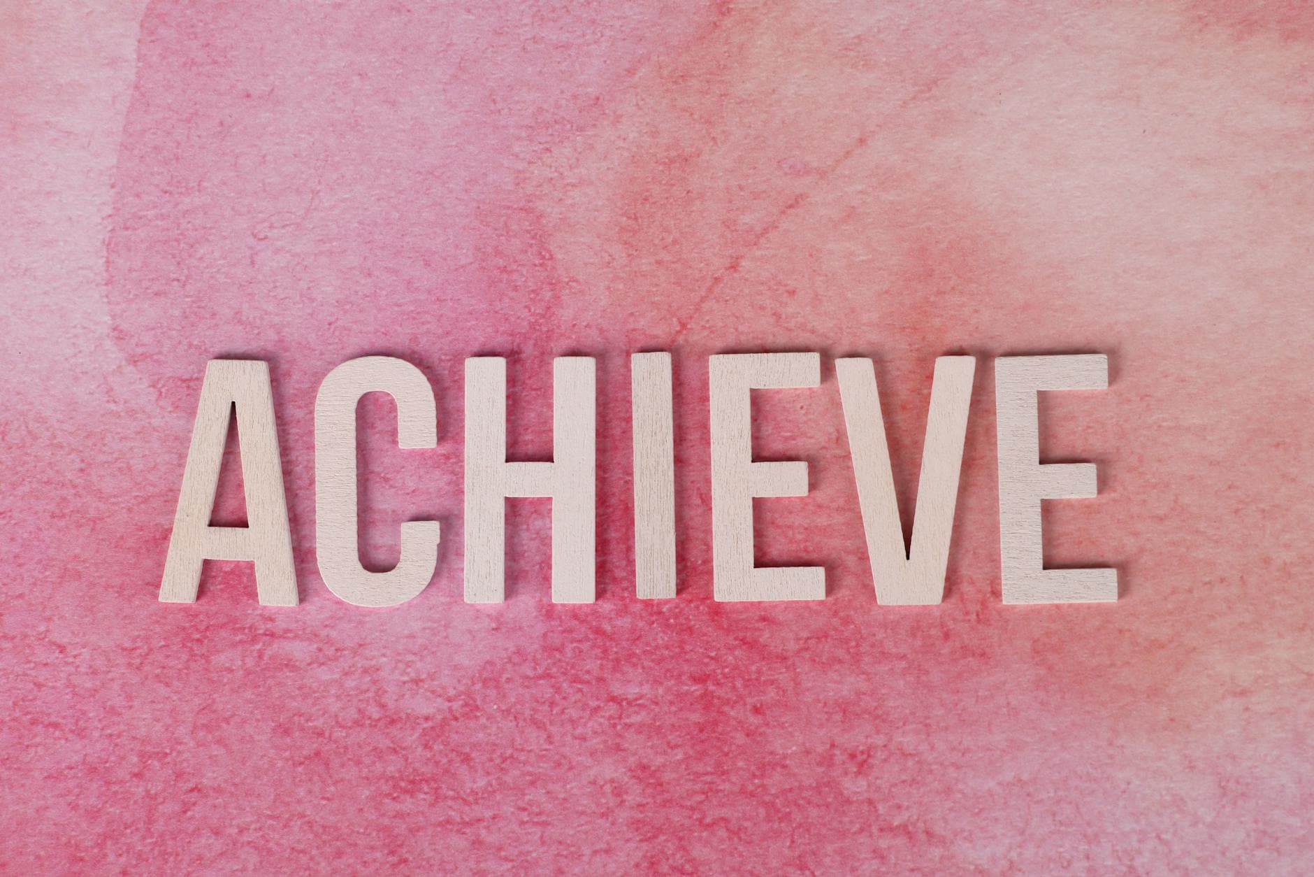The word 'Achieve' in wooden letters on a textured pink background, symbolizing success and motivation. - achievable therapy goals
