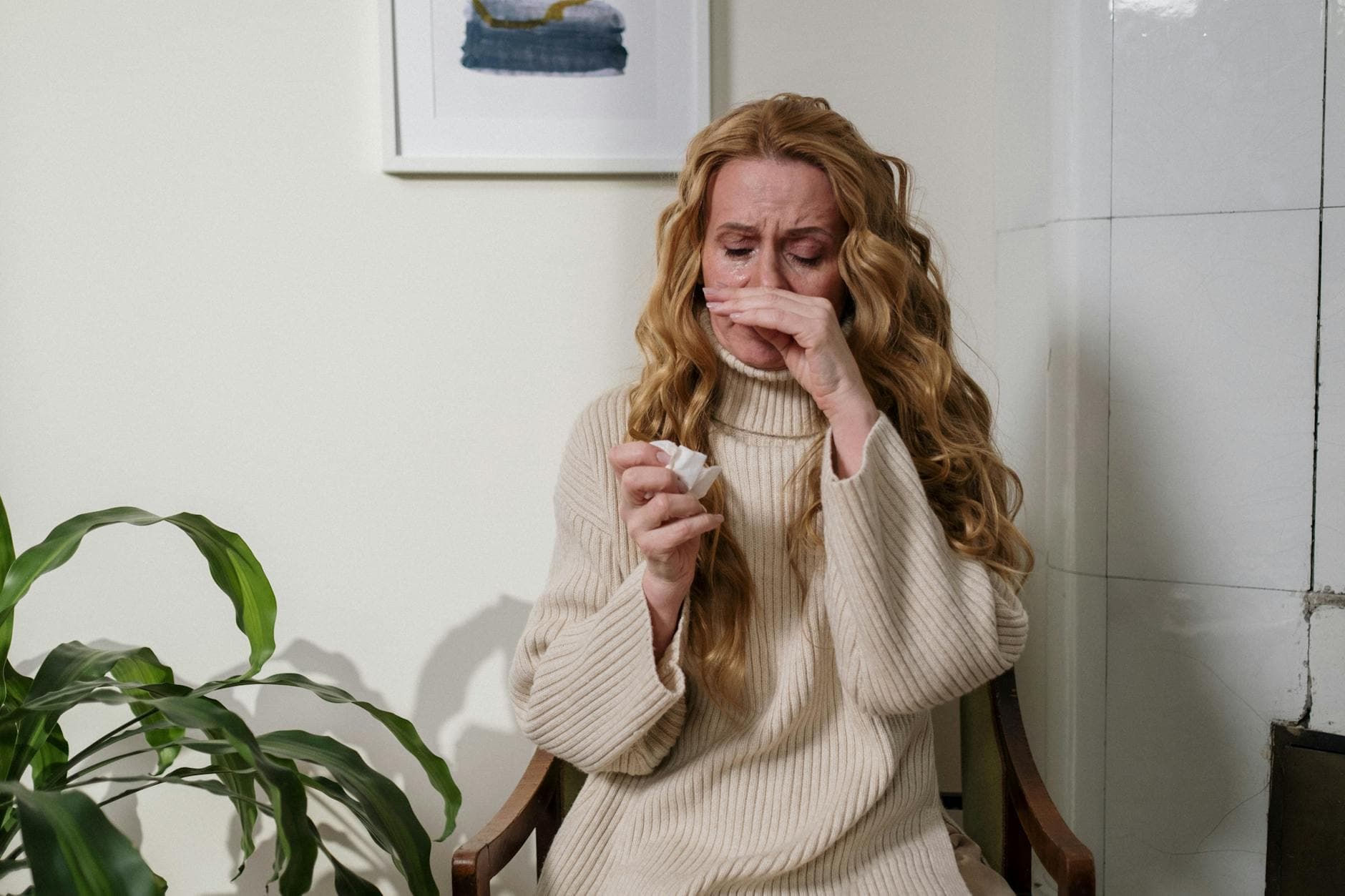 A woman with a runny nose sitting indoors, using a tissue to relieve her allergies. - allergies mood focus
