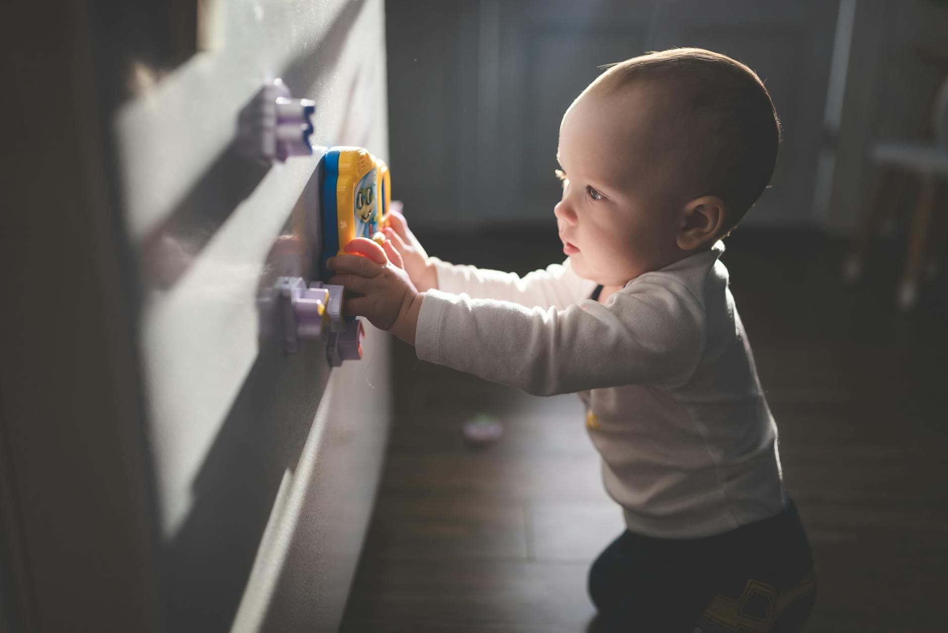 A cute baby exploring magnetic toys on a cupboard, illuminated by natural light indoors. - child growth spurts