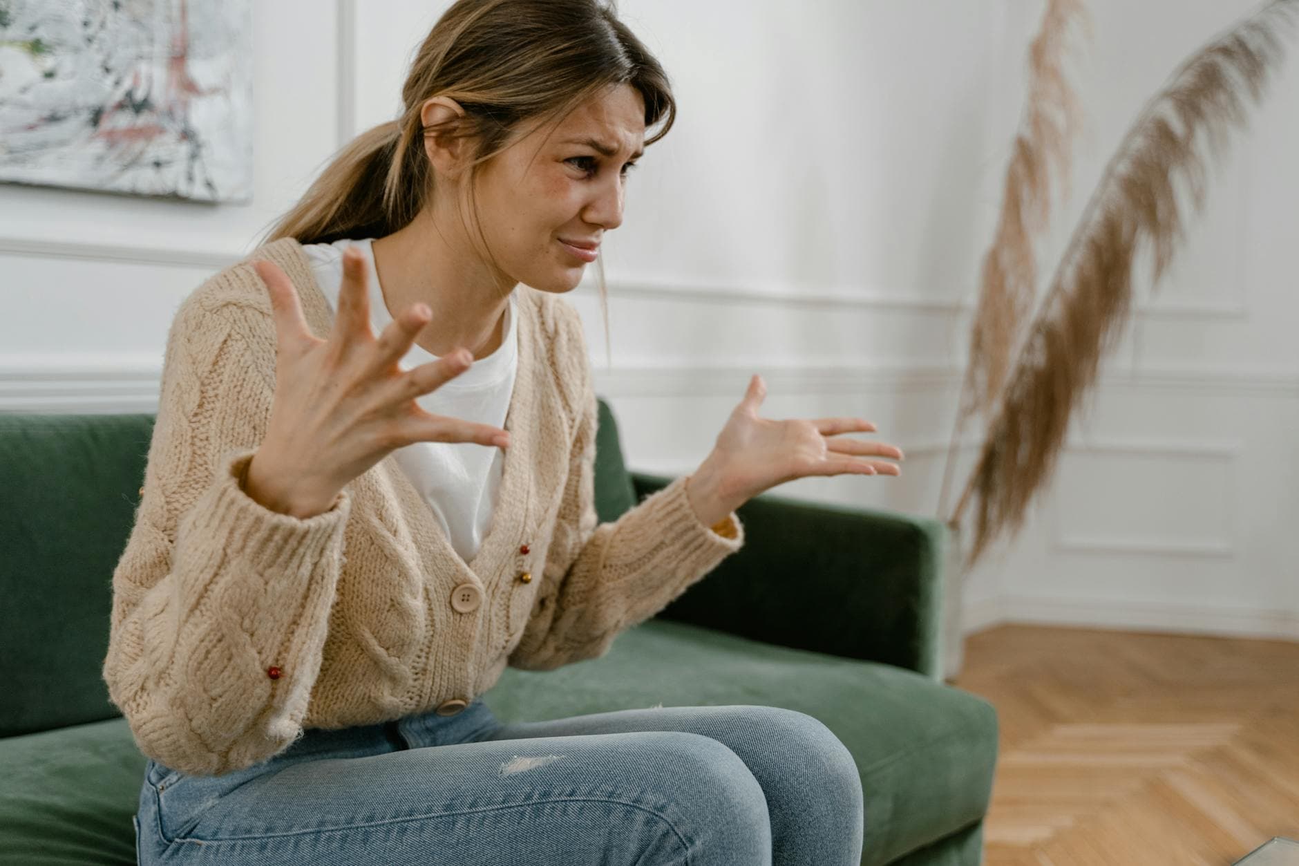 A woman sitting on a green sofa, gesturing emotionally, indoors. - let go of past hurts