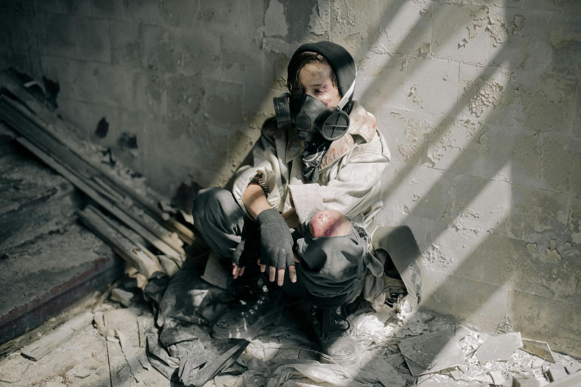A young person in a gas mask sits in a decaying, abandoned building, evoking themes of survival and desolation. - post winter loneliness