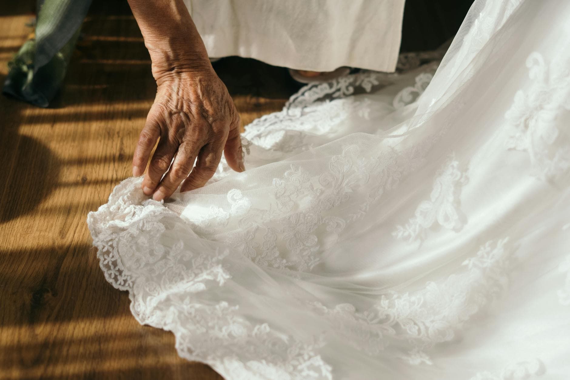 A senior adult hand gently adjusts delicate lace on a wedding dress in soft lighting. - pre-marriage counseling