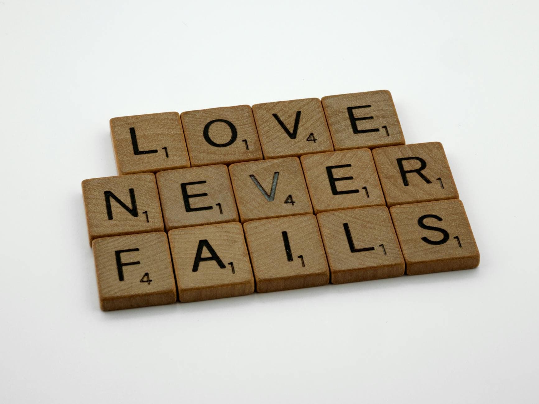 Wooden Scrabble tiles spelling out 'Love Never Fails' on a white background. - self-compassion after failed resolutions