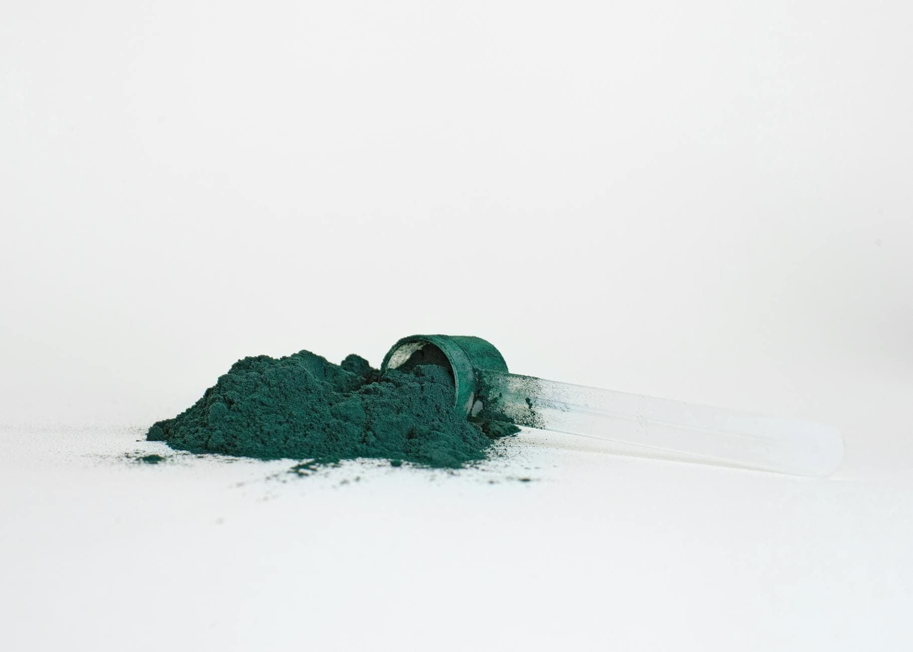 A pile of spirulina powder in a transparent measuring scoop isolated on a white background. - spring energy boost
