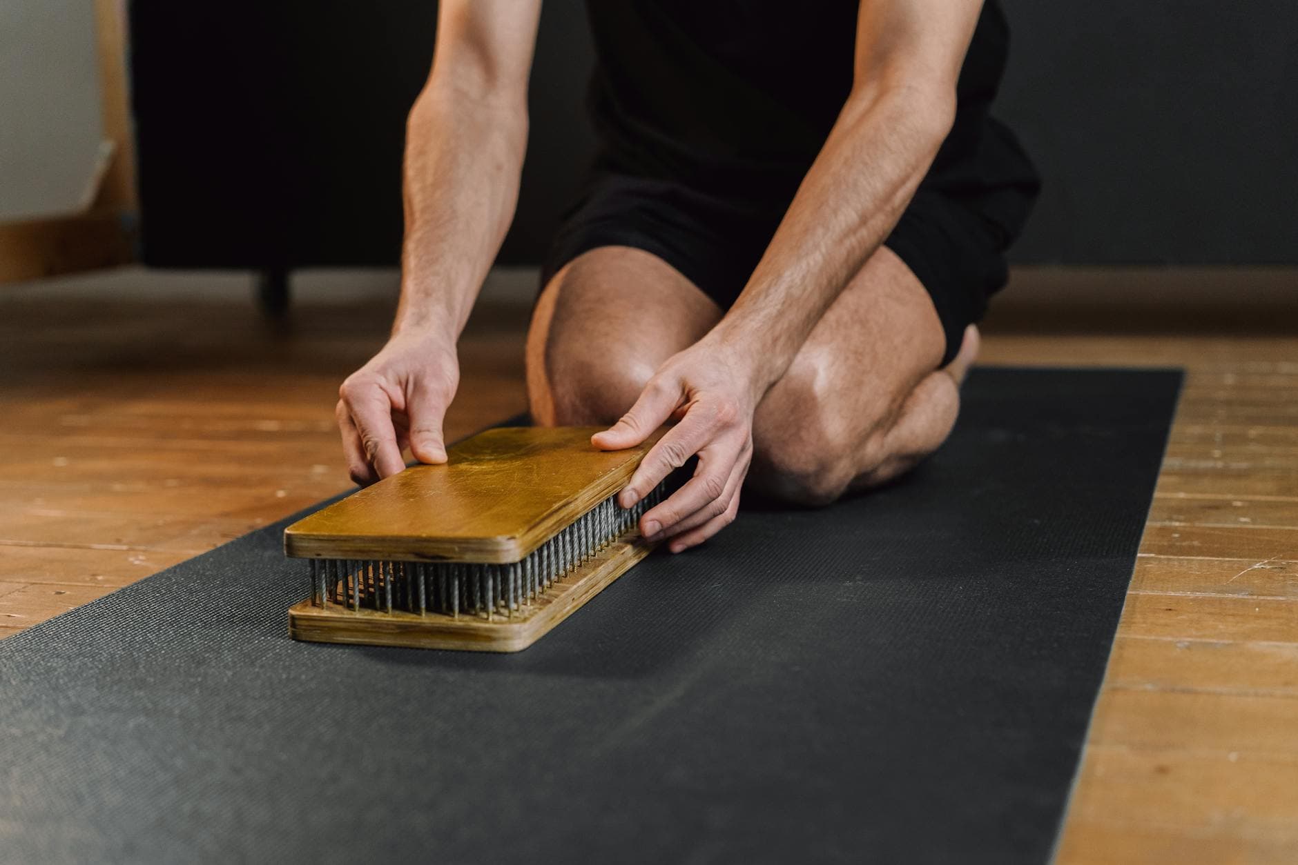 A man sets up a wooden meditation board on a yoga mat indoors, highlighting mindfulness practice. - spring mental clarity
