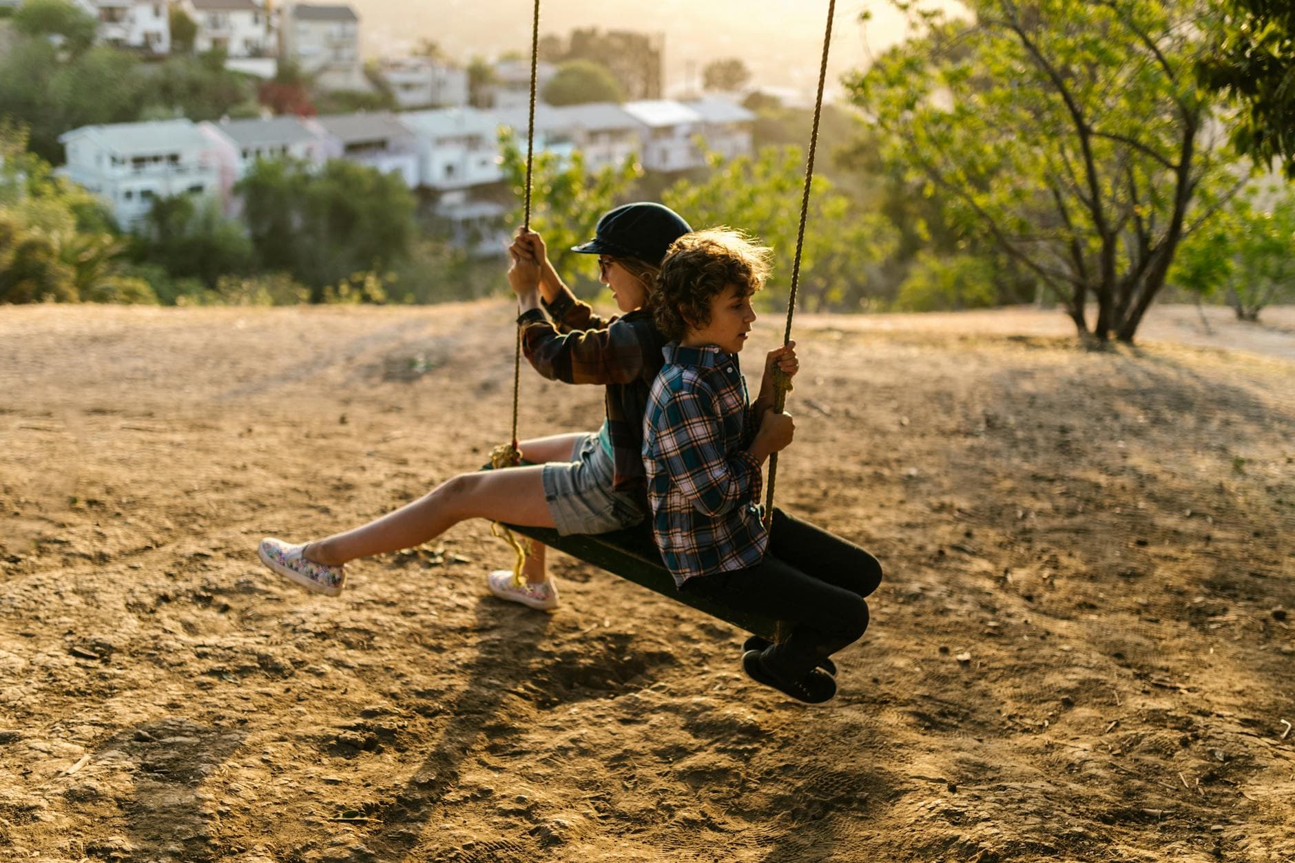 Two children enjoy a playful swing ride outdoors at sunset. - spring mood swings