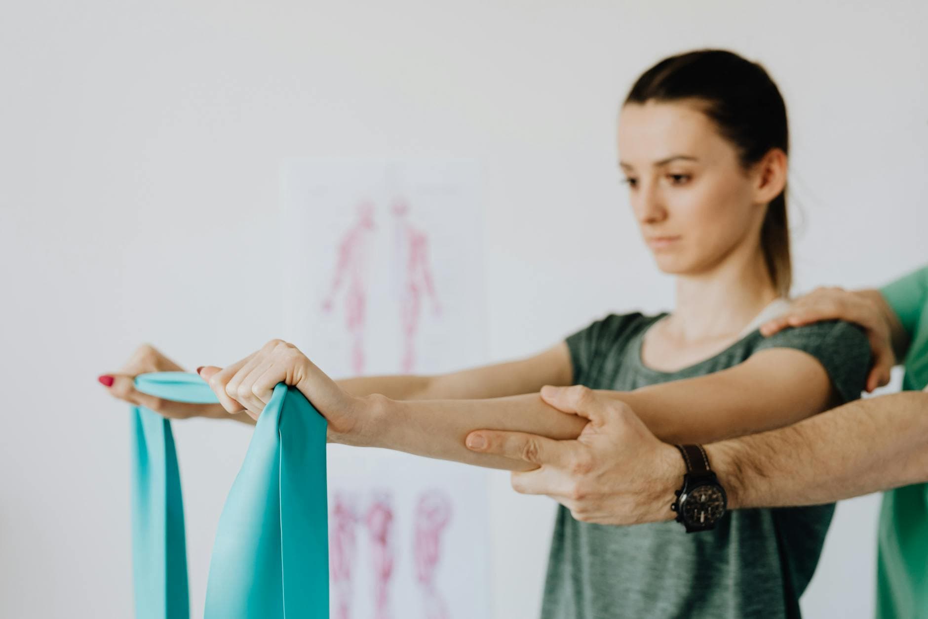 Slim young female in casual wear standing with reached arms and elastic tape during medical checkup by crop unrecognizable osteopath in wristwatch - spring procrastination therapy