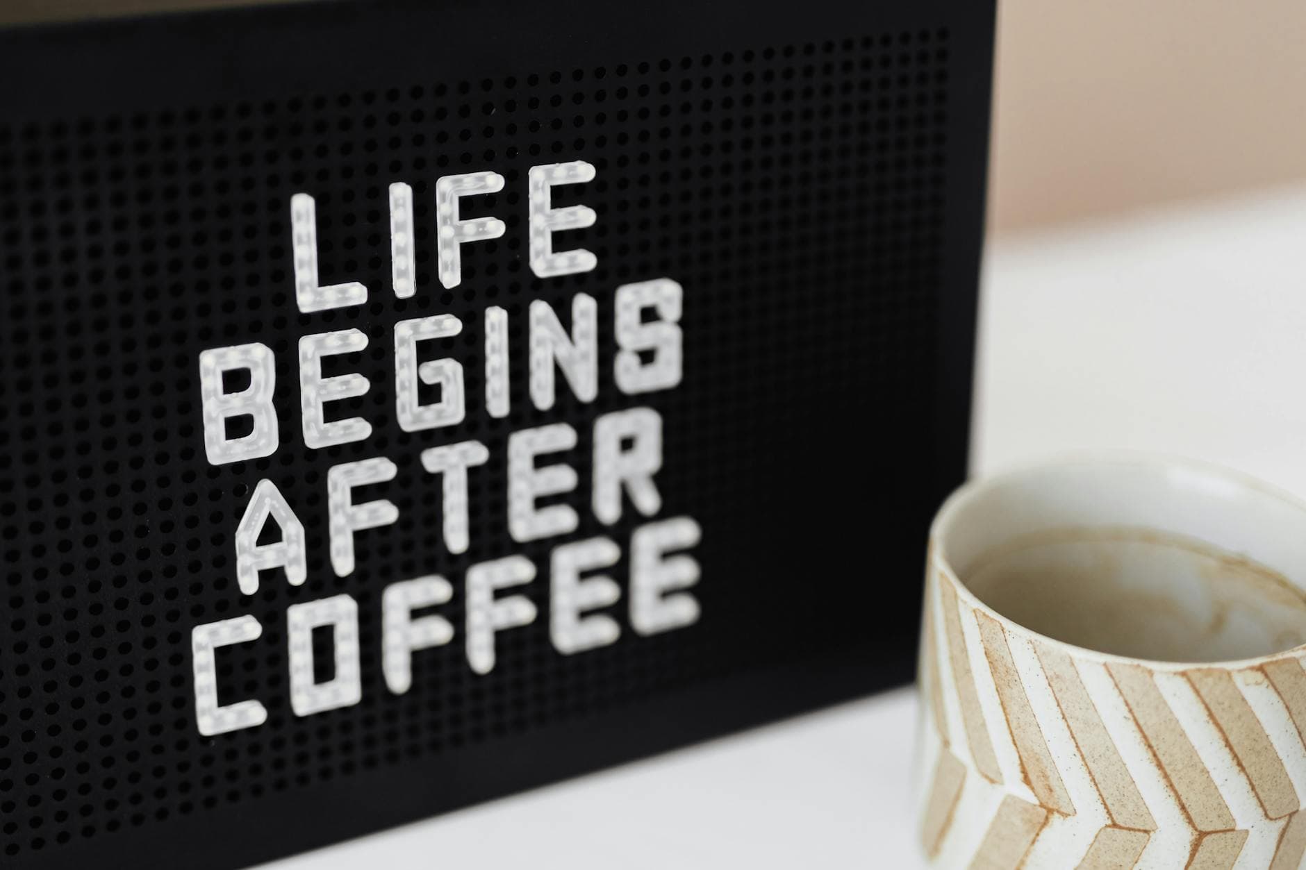 Peg message board with Life Begins After Coffee motto and empty ceramic cup of coffee with creative striped design on white table - start dating after divorce