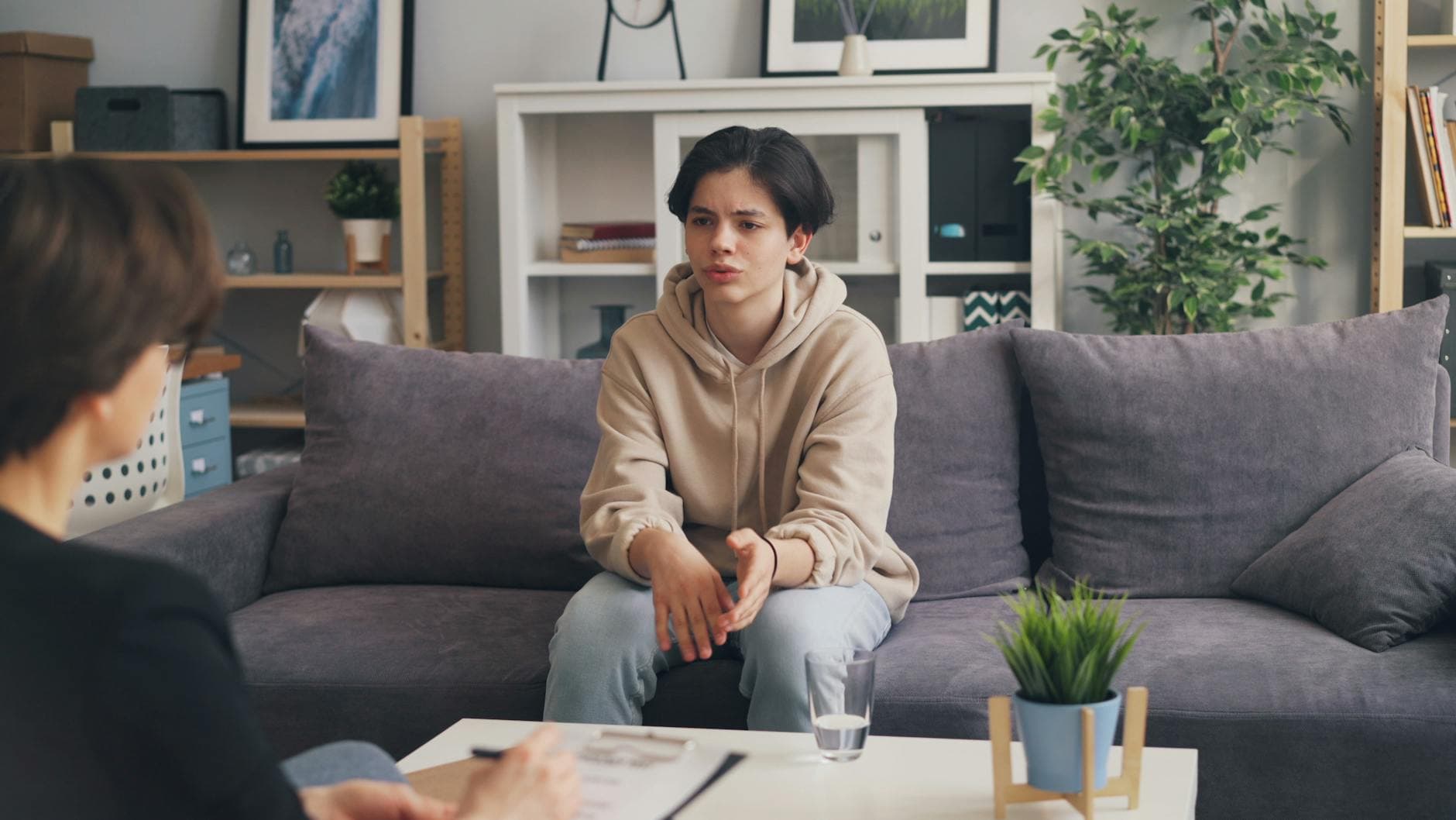 Teenager attending therapy session in a modern office, expressing emotions. - teen mental health
