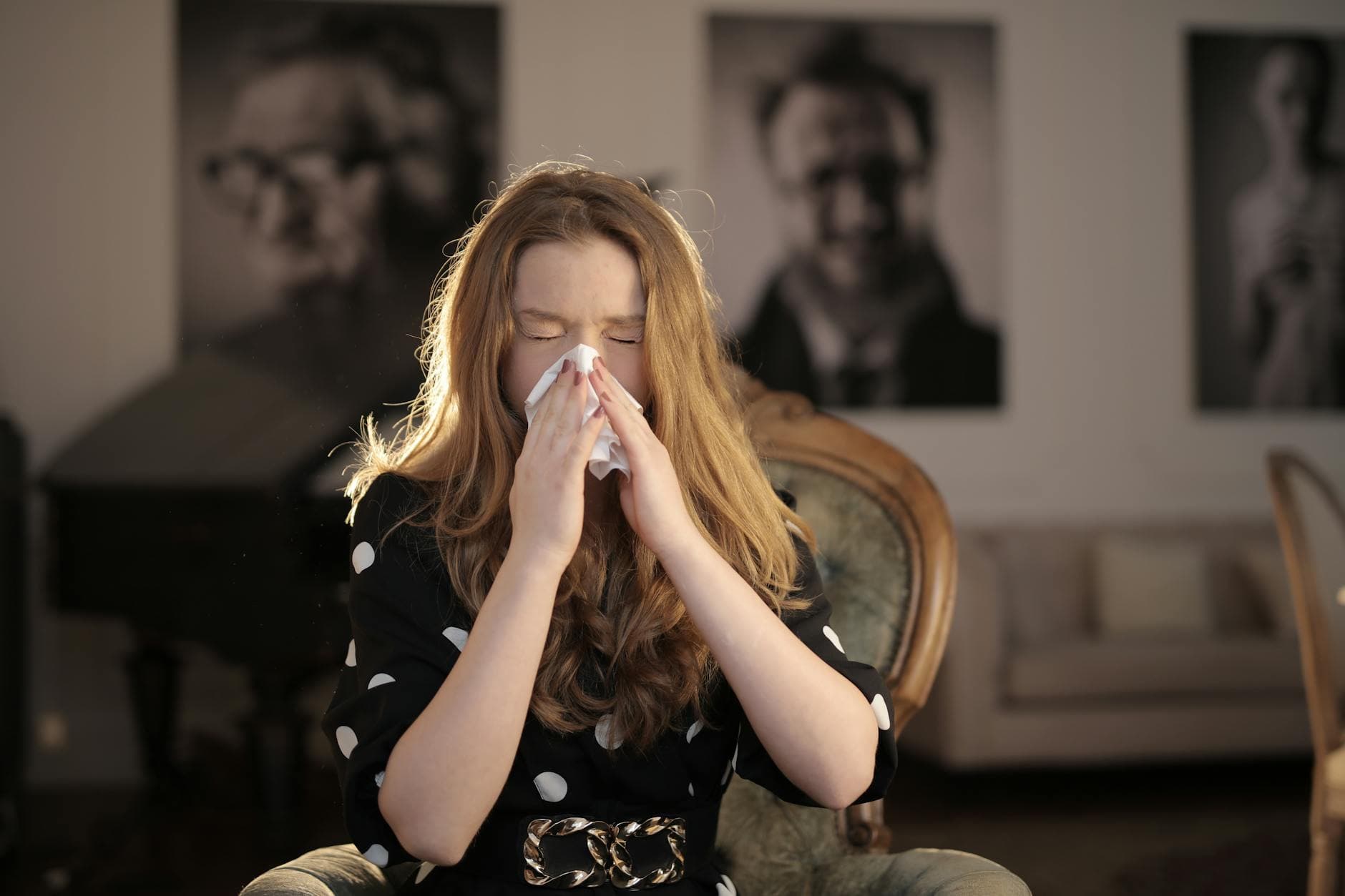 A young woman with closed eyes sneezing into a tissue, sitting indoors. - teen spring allergies
