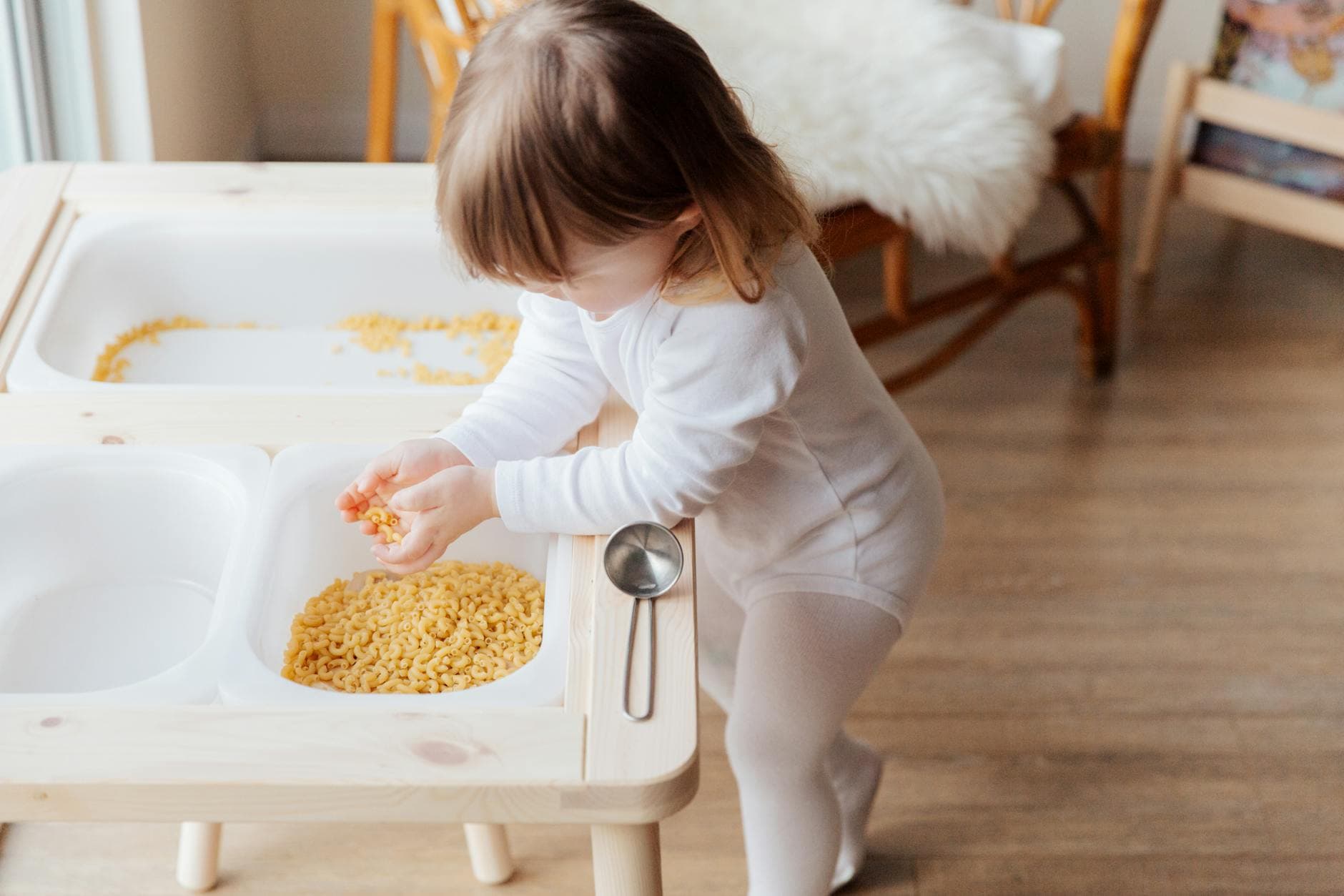 A young child playing with dry pasta in an indoor setting, exploring textures. - toddler spring activities