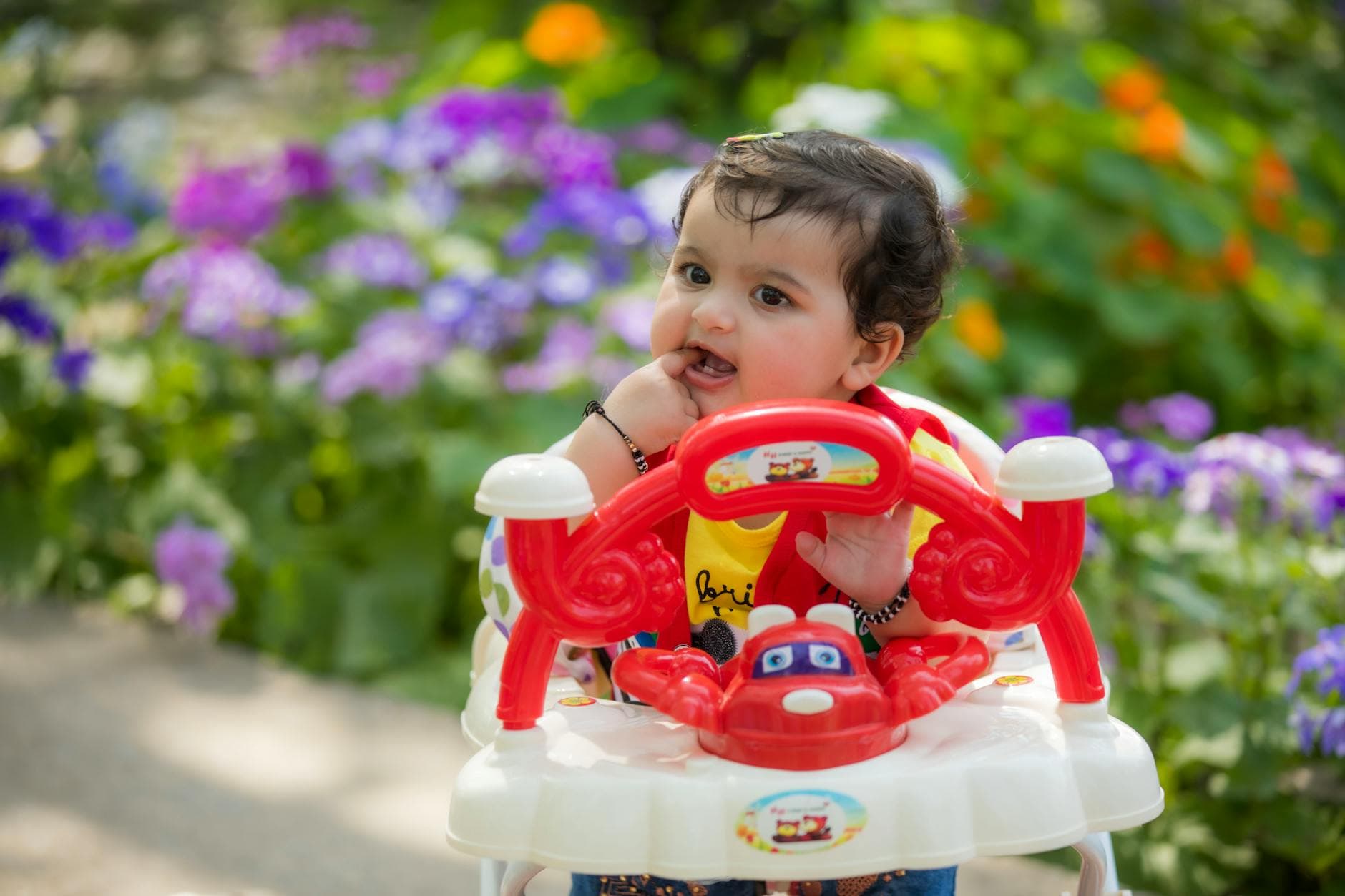 Charming baby in a walker enjoys a sunny day in a vibrant garden full of colorful flowers. - toddler spring allergies