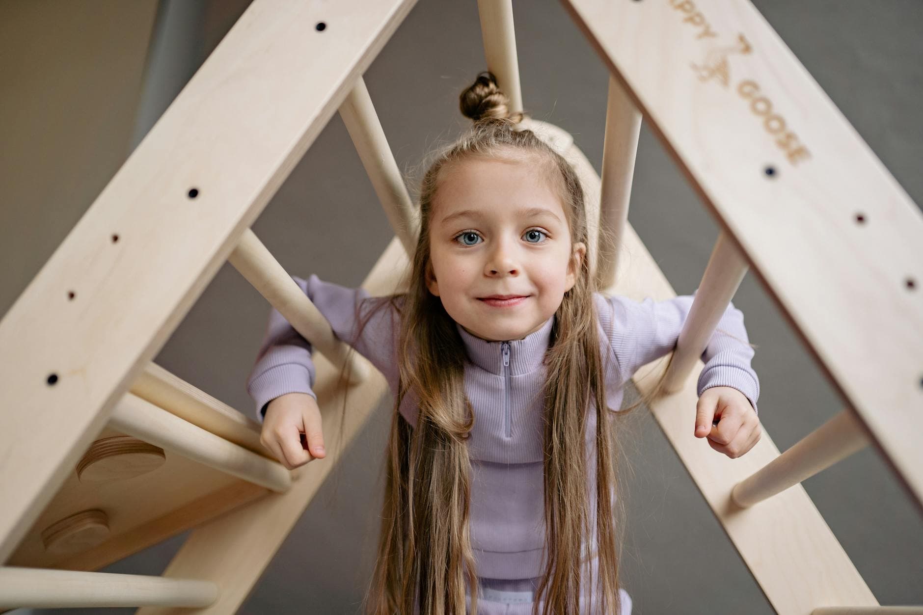 A cheerful young girl in a purple outfit climbs a wooden ladder with a smile. - toddler spring energy