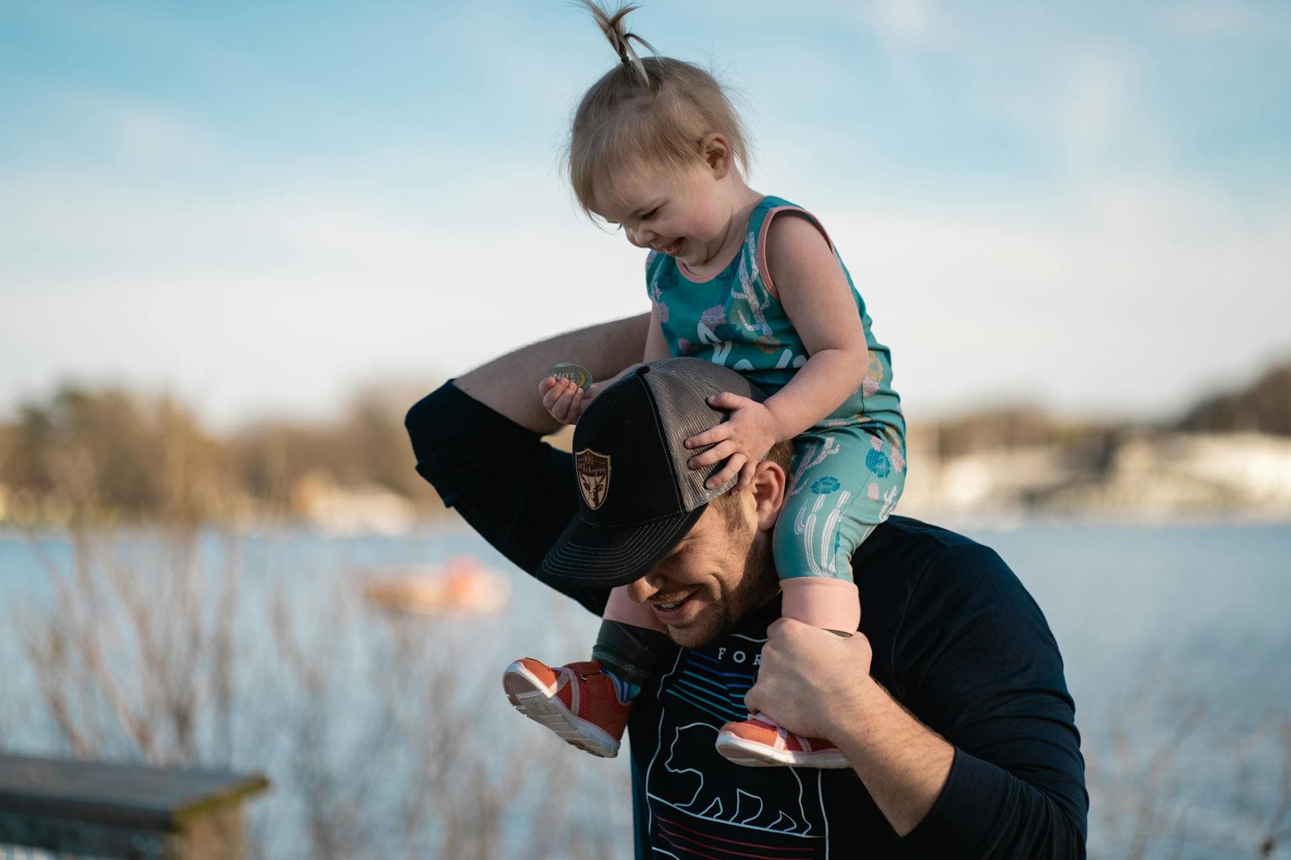 Father carrying daughter on shoulders by the lake, sharing a joyful moment together. - toddler spring tantrums