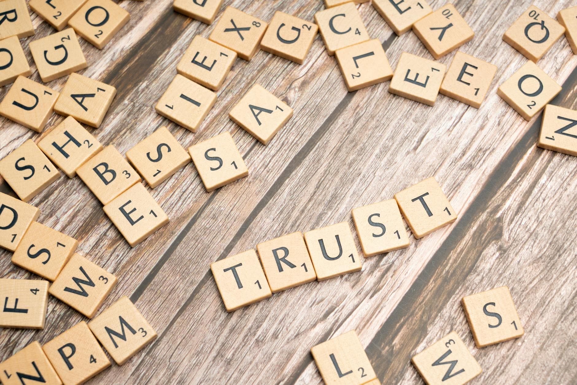 Scrabble letter tiles form the word 'Trust' on a wooden table, surrounded by scattered tiles. - build trust partner