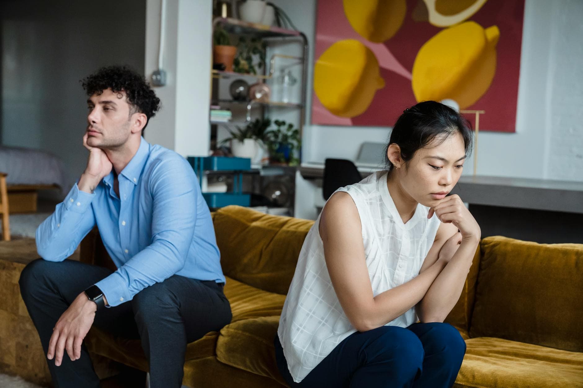A couple sits indoors on a sofa, both appearing thoughtful and contemplative. - couple communication needs