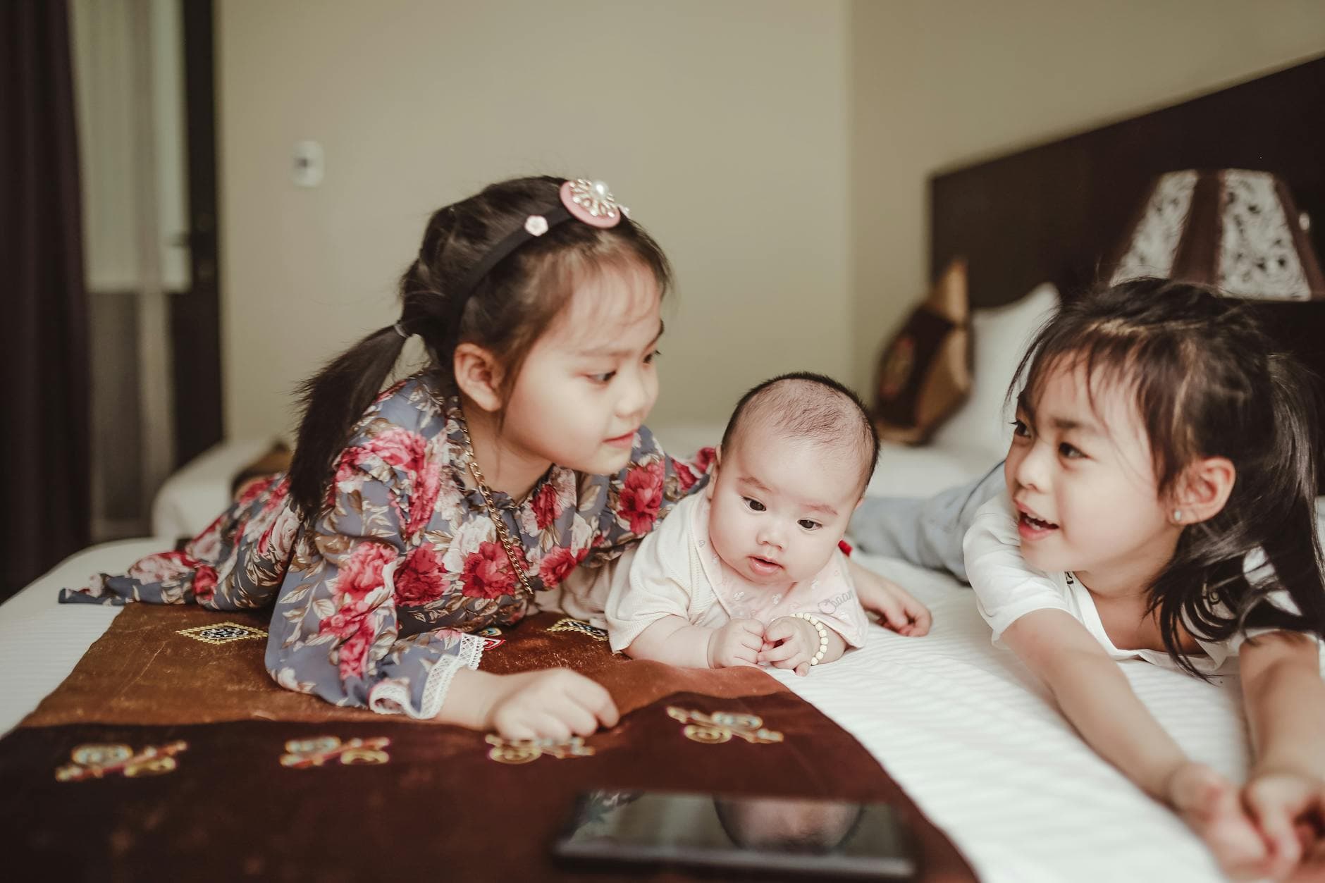 Adorable Asian smiling little girls cuddling newborn baby lying on white delicate blanket on bed in bedroom - family guy sibling rivalry