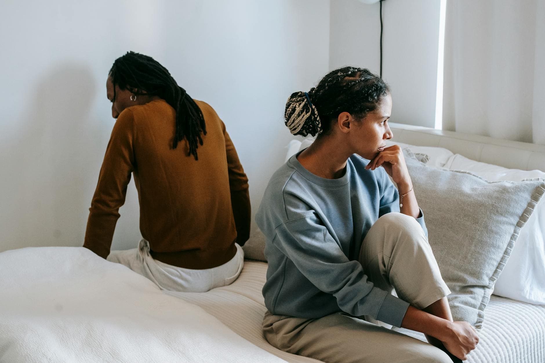 Young discontented African American female touching chin near anonymous male partner during dispute in bedroom - relationship needs communication