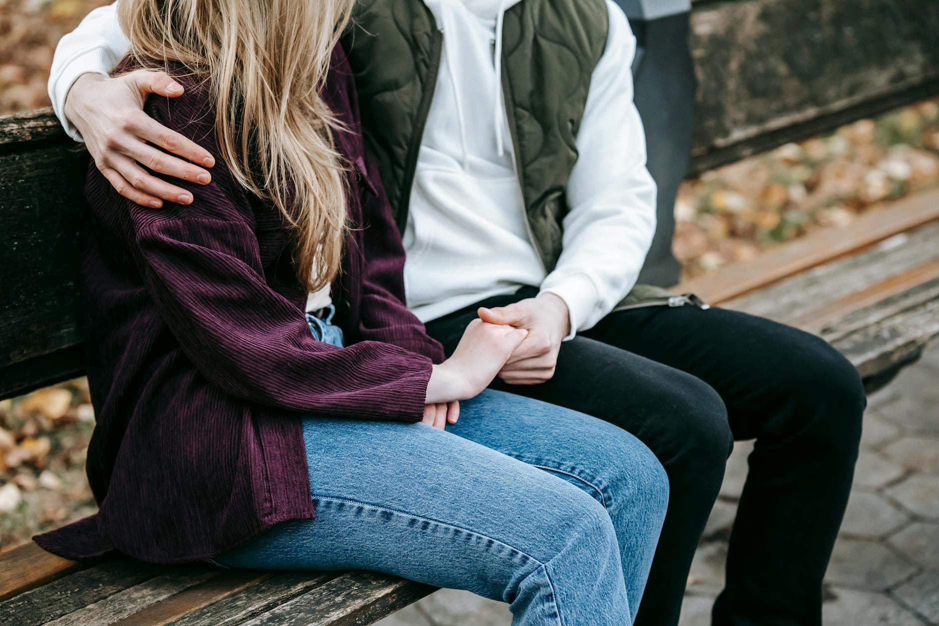Crop anonymous tender young couple in casual stylish outfit cuddling and holding hands on wooden bench - release relationship resentments