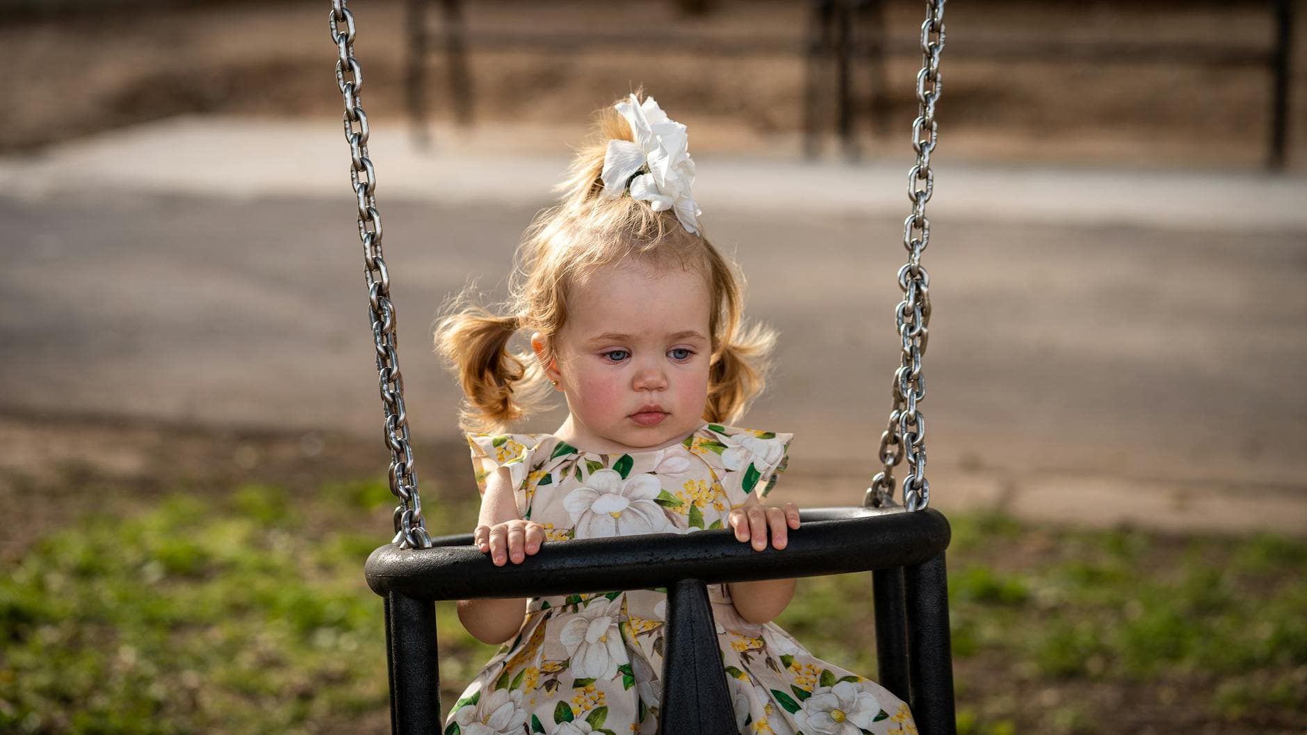 A cute toddler girl with pigtails and a floral dress on a swing in a sunny Los Angeles park. - seasonal mood swings