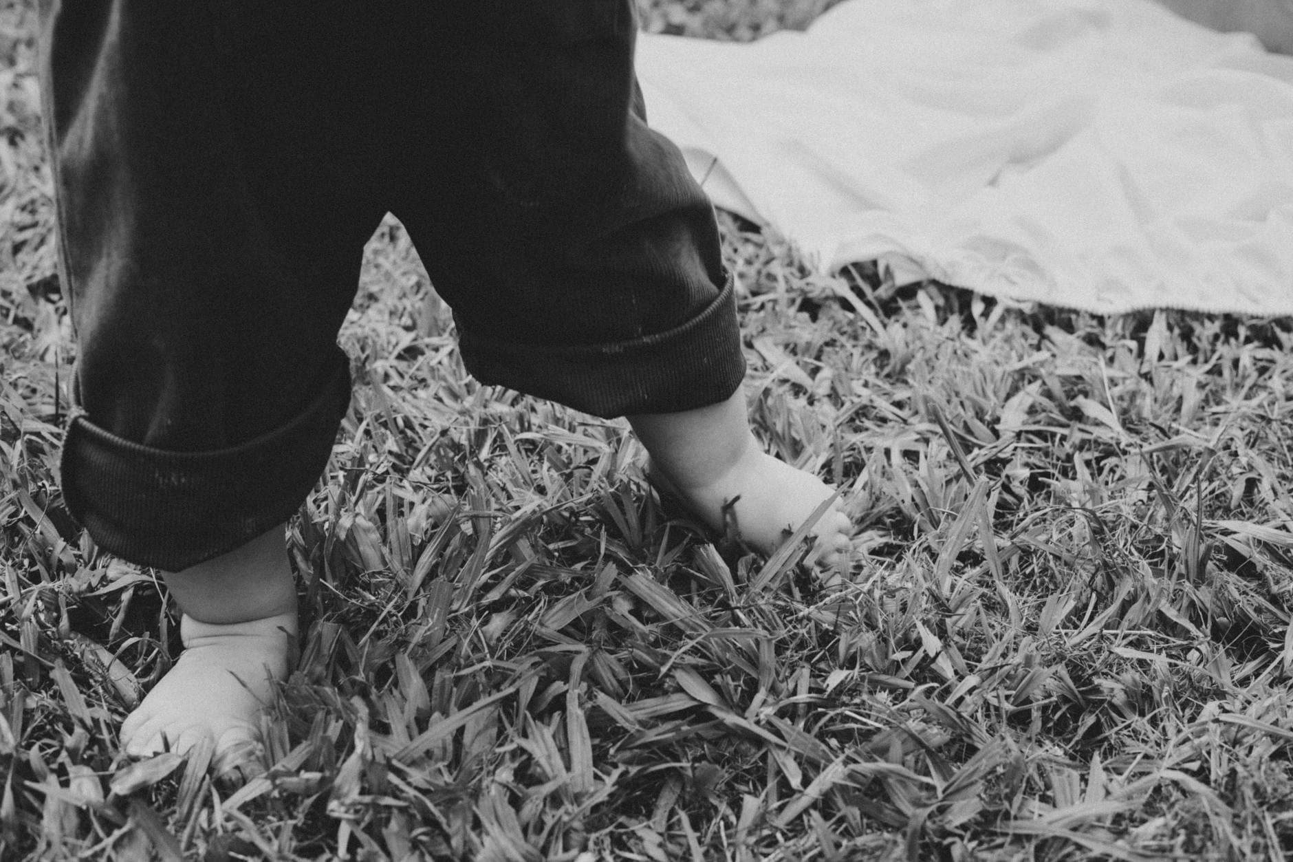 Black and white photo of a baby taking first steps on grass, showing feet and rolled-up pants. - toddler growth spurts