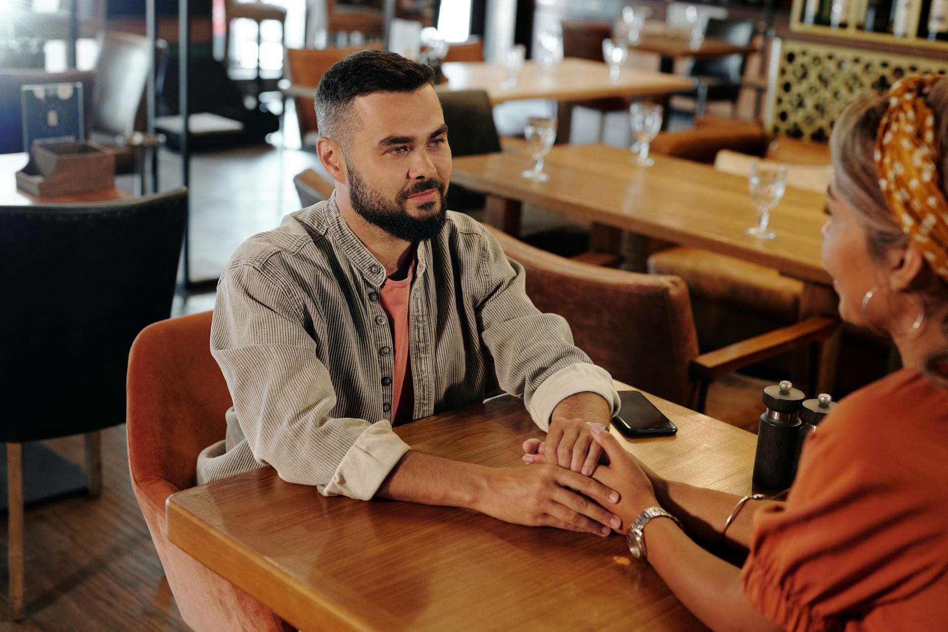 A couple enjoys a romantic moment holding hands at a cozy café, creating a warm atmosphere. - vulnerable dating