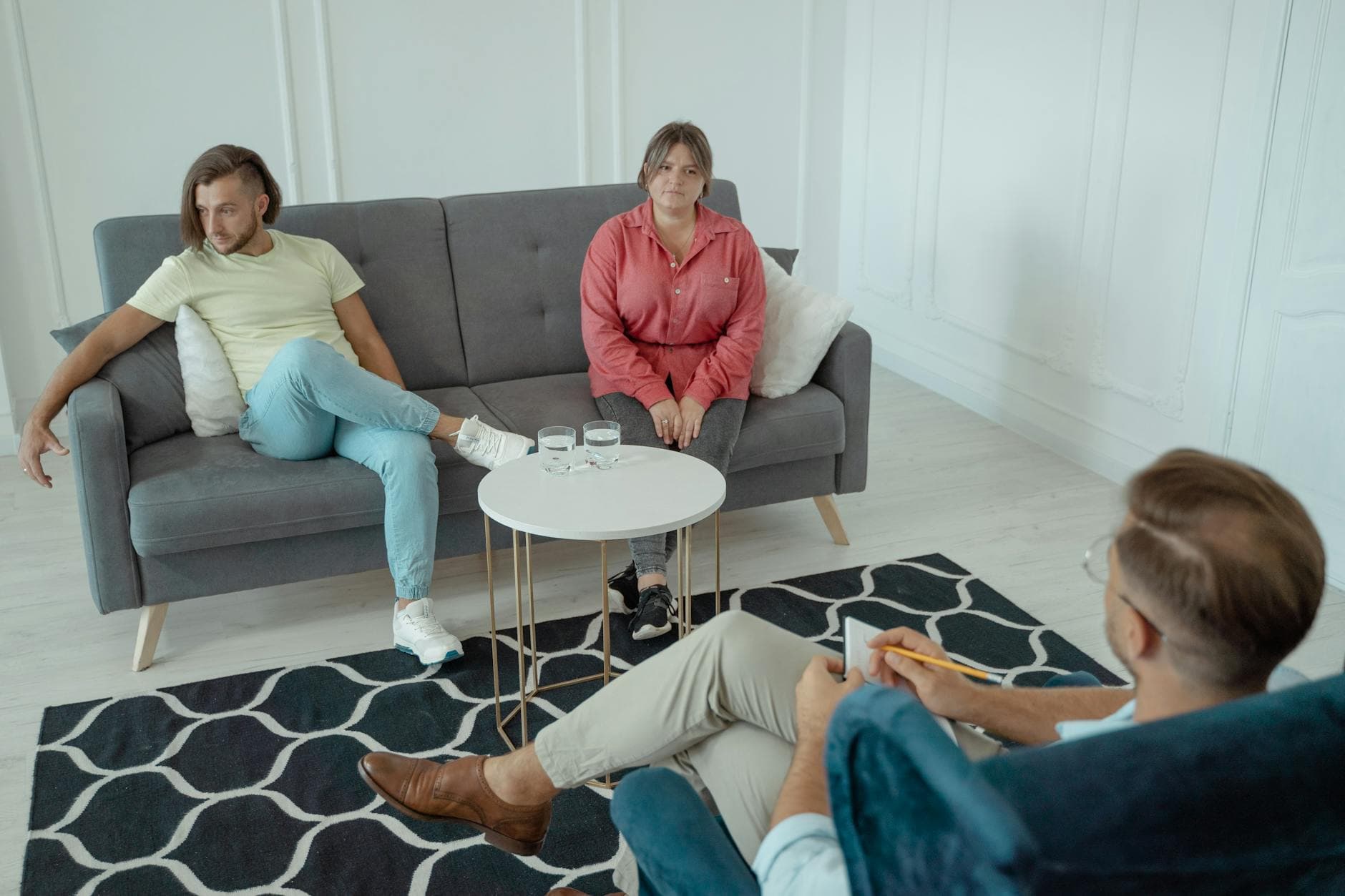 A couple attends a therapy session in a modern styled office setting, with a counselor sitting across from them. - couples therapy boredom