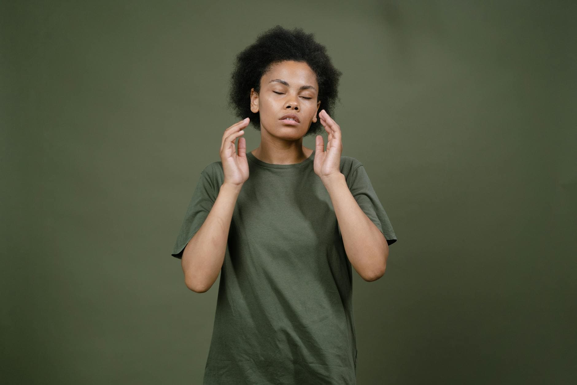 A serene woman with closed eyes and afro hair in a green shirt, appearing contemplative. - dbt emotional regulation