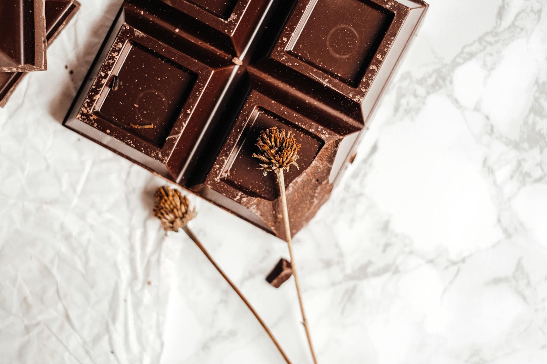 Close-up of a dark chocolate bar on marble with dried flowers, showcasing elegance in food photography. - natural mood boosters