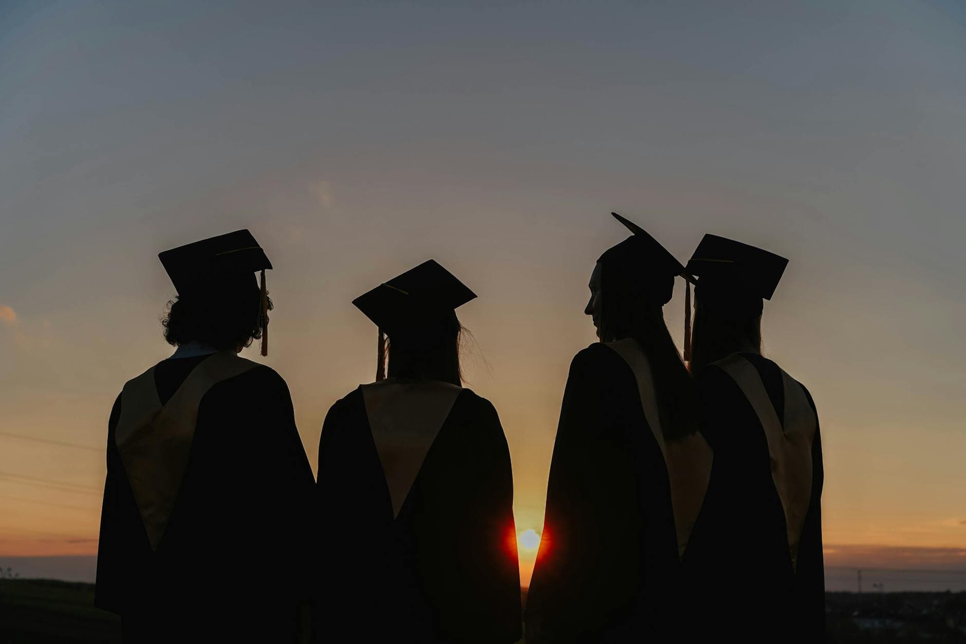 A group of graduates in caps and gowns silhouetted against a beautiful sunset, symbolizing achievement. - post grad relationships
