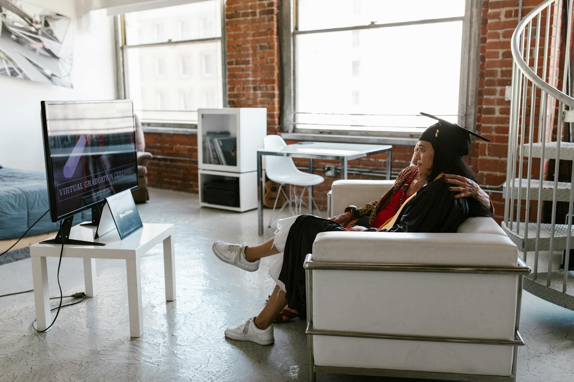 Two women celebrating a virtual graduation at home in a cozy apartment setting. - post grad resilience