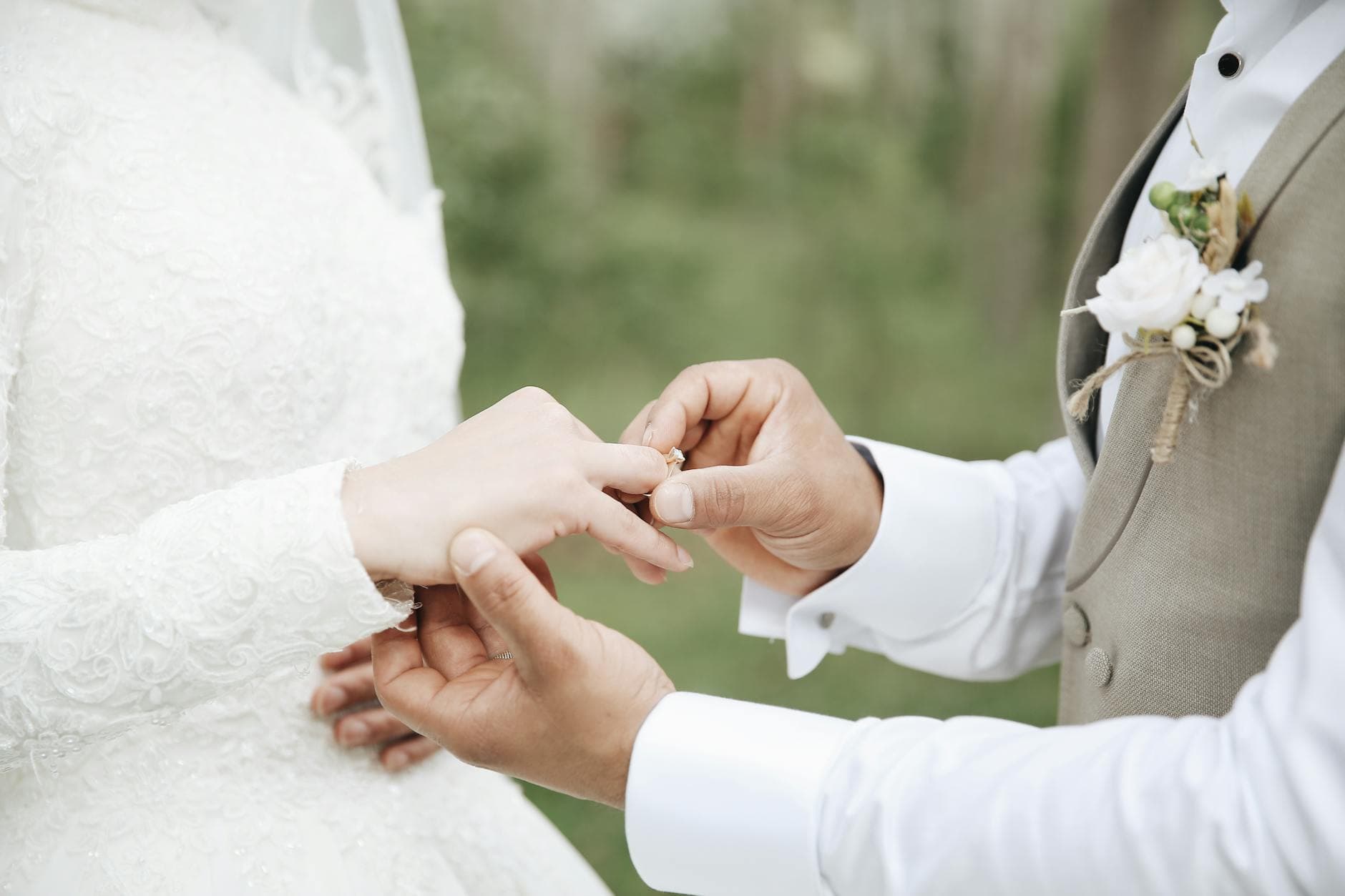 Close-up of a groom placing a wedding ring on the bride's finger during an outdoor ceremony. - spring wedding survival