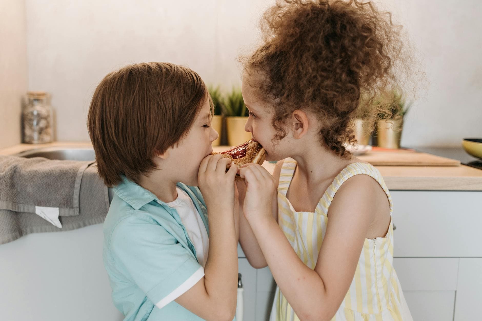 Two children sharing a jam sandwich, having fun in a cozy kitchen setting. - teaching toddlers sharing