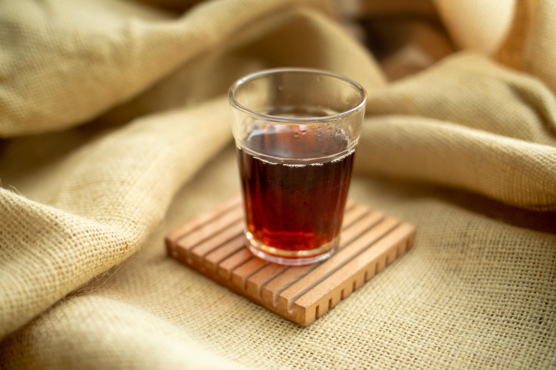 A clear glass filled with warm tea resting on a wooden coaster and burlap fabric. - anger management near me
