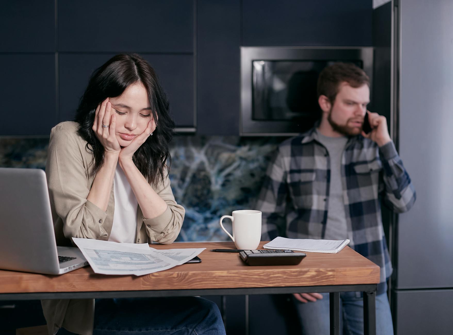 A couple dealing with financial stress, surrounded by bills and a laptop indoors. - anxiety in romantic relationships