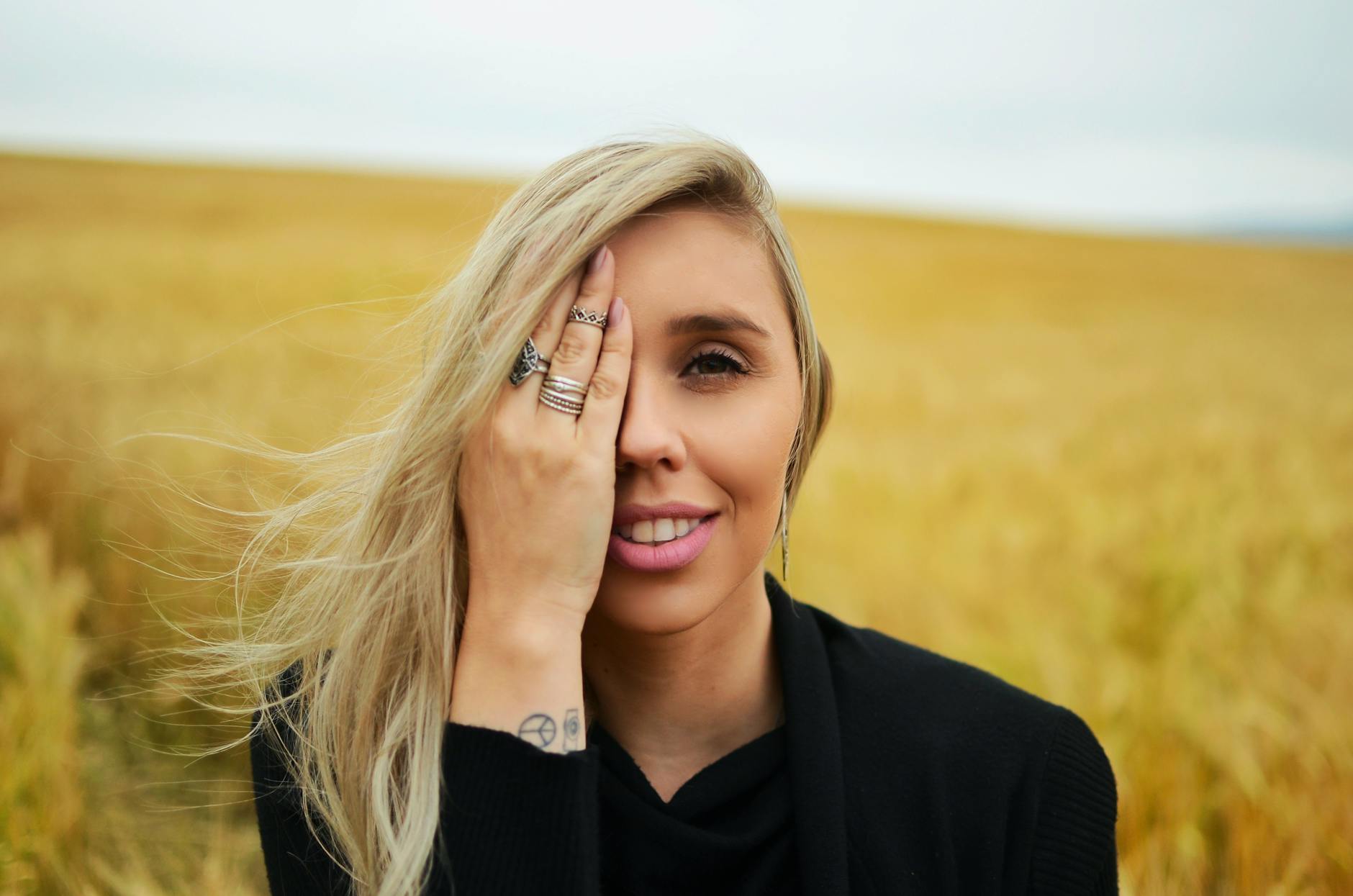 Young woman with blonde hair smiling, covering face in a field. Warm tones and natural setting. - anxiety symptom checklist